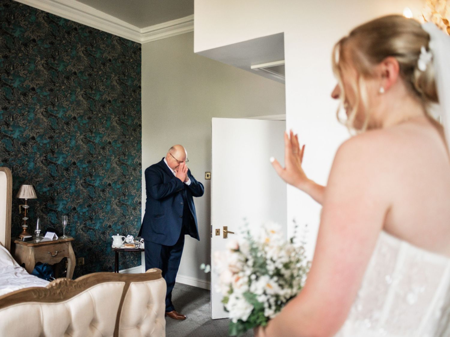 First look moment in a luxurious hotel room with ornate wallpaper.