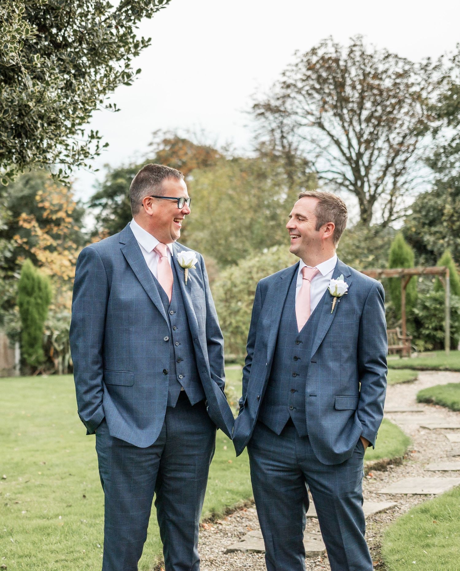Two people in blue suits sharing a moment outdoors in a garden setting.