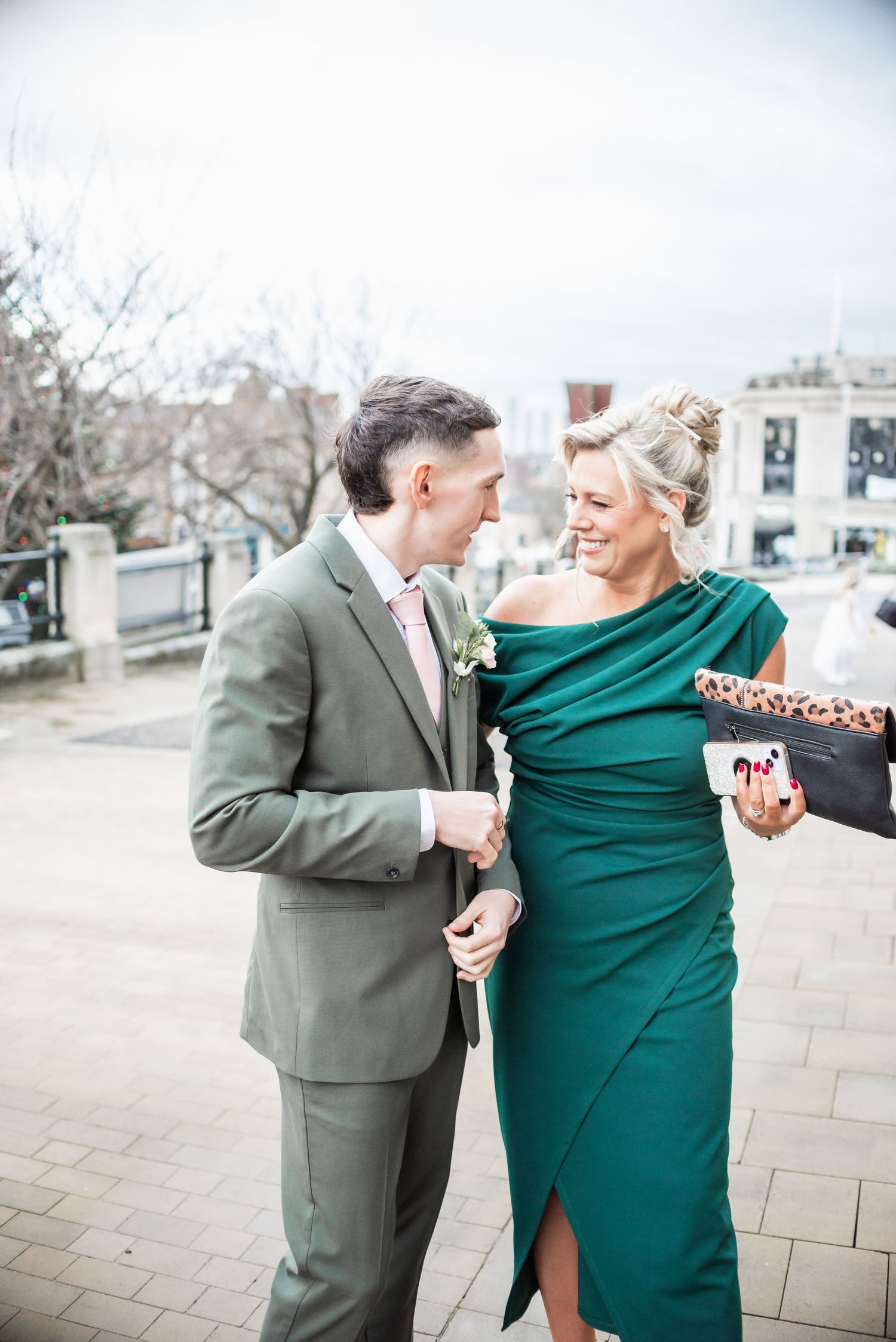 Elegantly dressed couple sharing a joyful moment outdoors in formal attire.