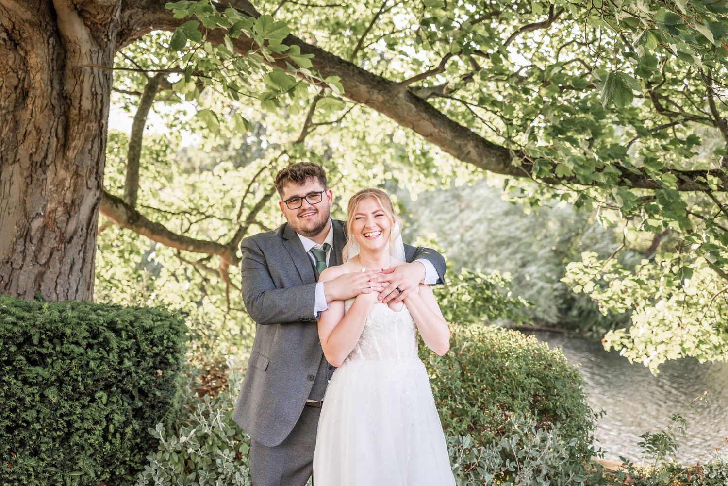 Newlyweds share a romantic moment under a large tree in an outdoor garden setting.