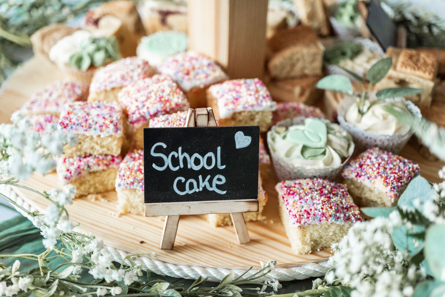 School cake treats decorated with pink sprinkles and eucalyptus on wooden serving board.