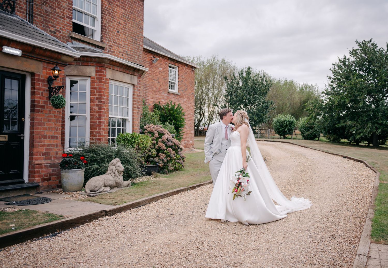 Panoramic view of a brick wedding venue with gravel path and garden surroundings.