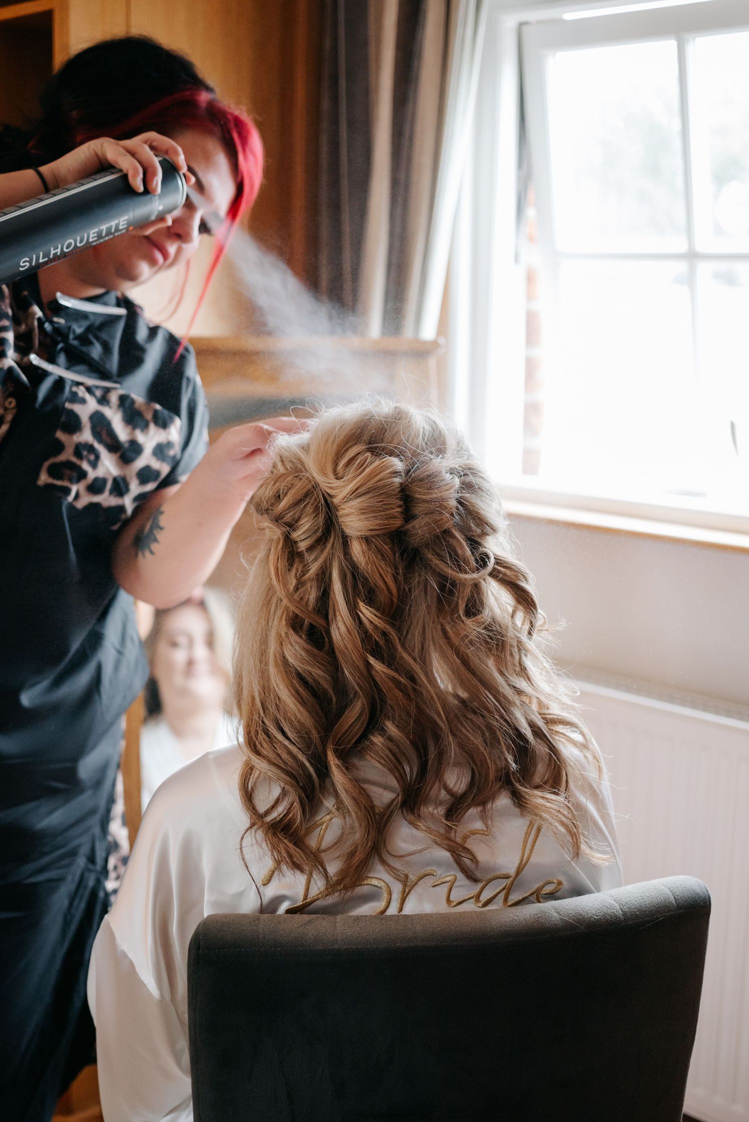 Hair stylist applying finishing touches and hairspray to an elegant updo hairstyle in preparation for a special event.