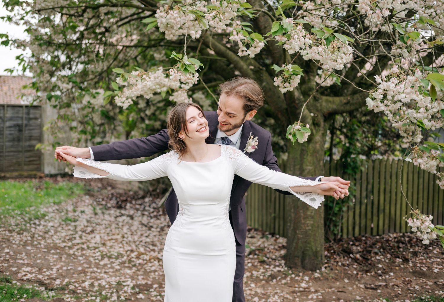 A romantic wedding moment captured under blooming white spring blossoms in a garden setting.