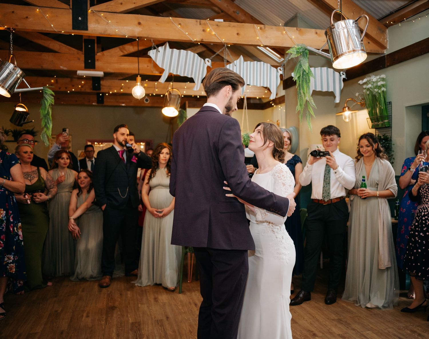 Wedding reception dance floor scene with exposed wooden beams and string lights overhead.