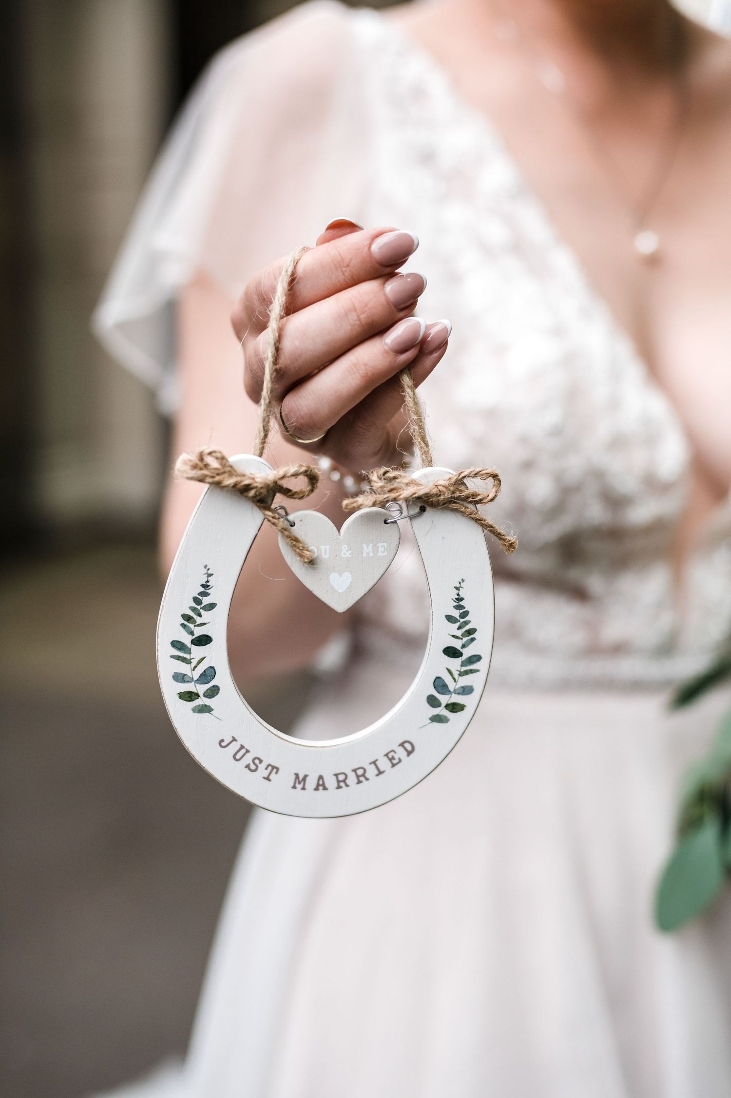 A decorative white horseshoe wedding ornament with floral design held by hands in a lace dress.