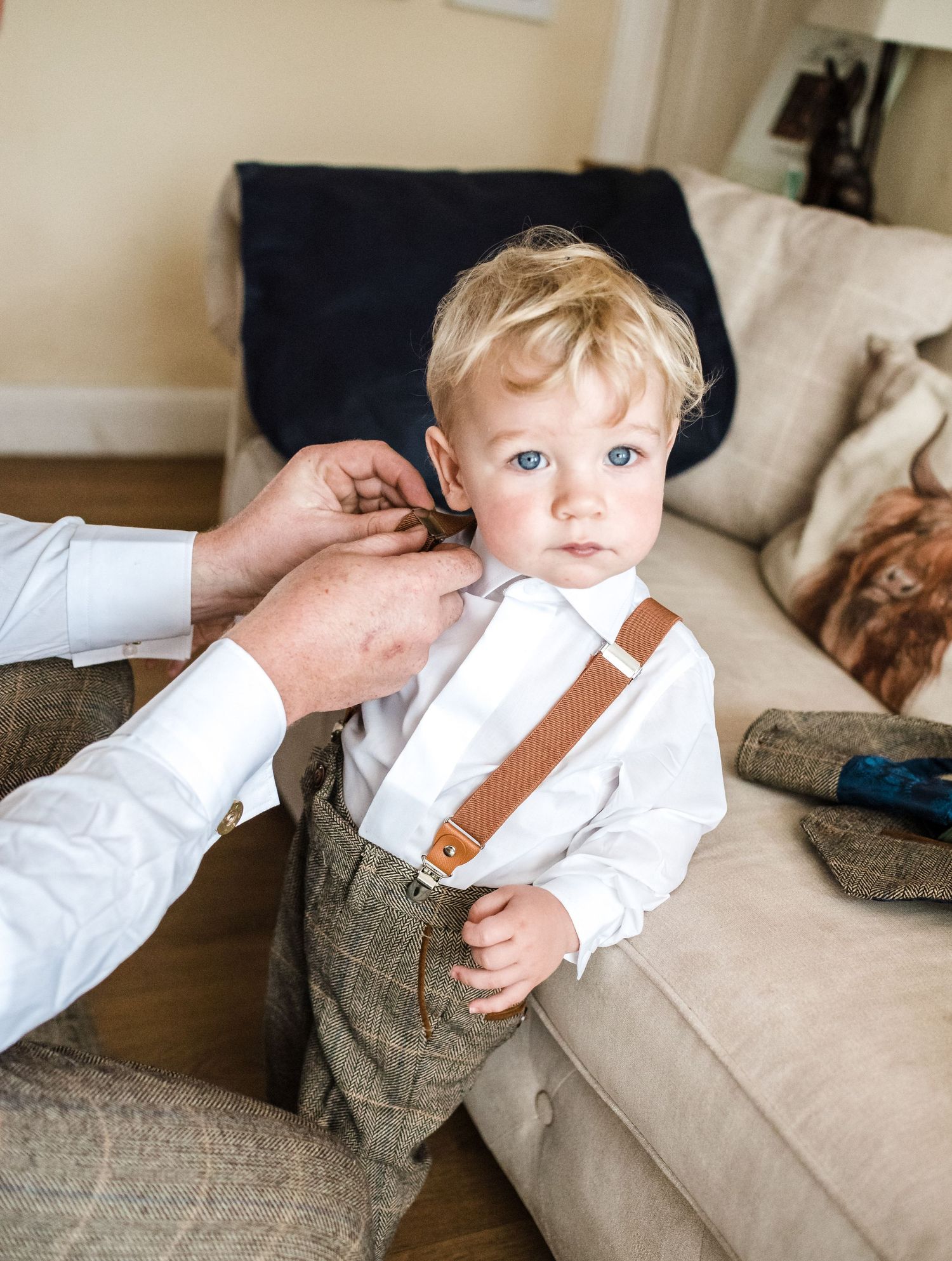 Small child in formal attire gets help with bow tie while wearing suspenders.