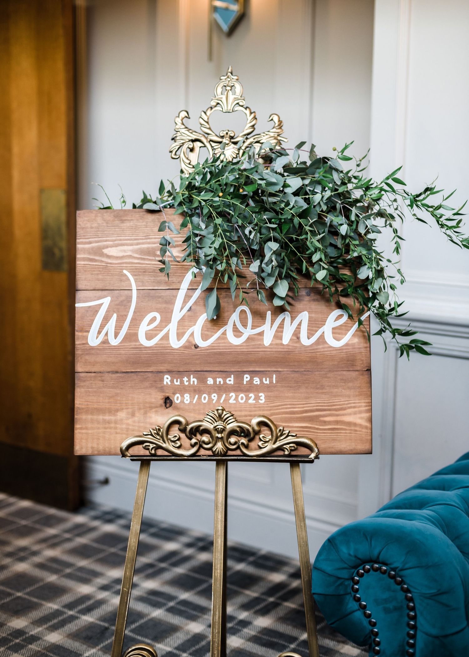Wooden welcome sign with gold crown detail and greenery decoration on gold easel.