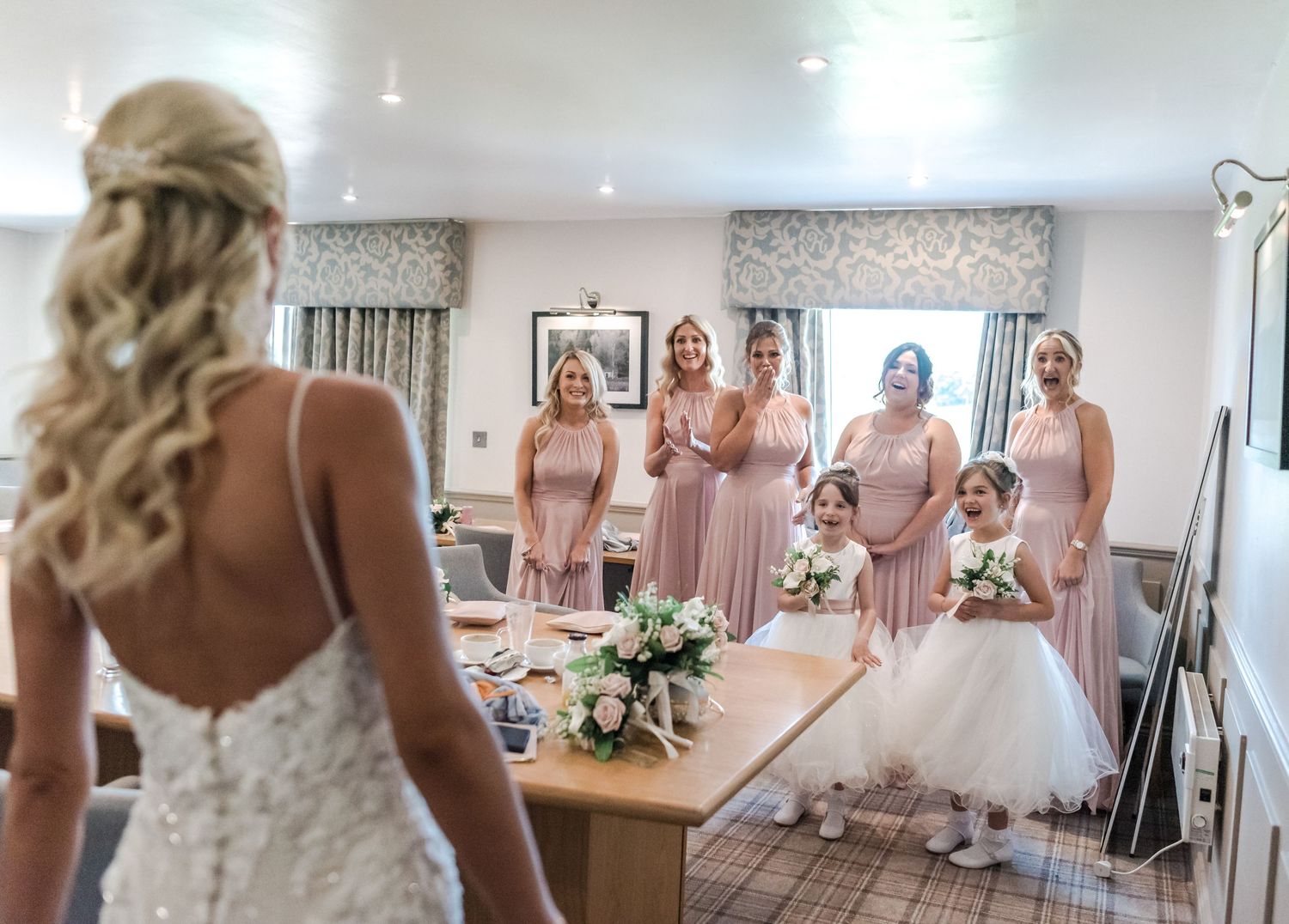 Wedding party in pink bridesmaid dresses gathered in a bridal suite.