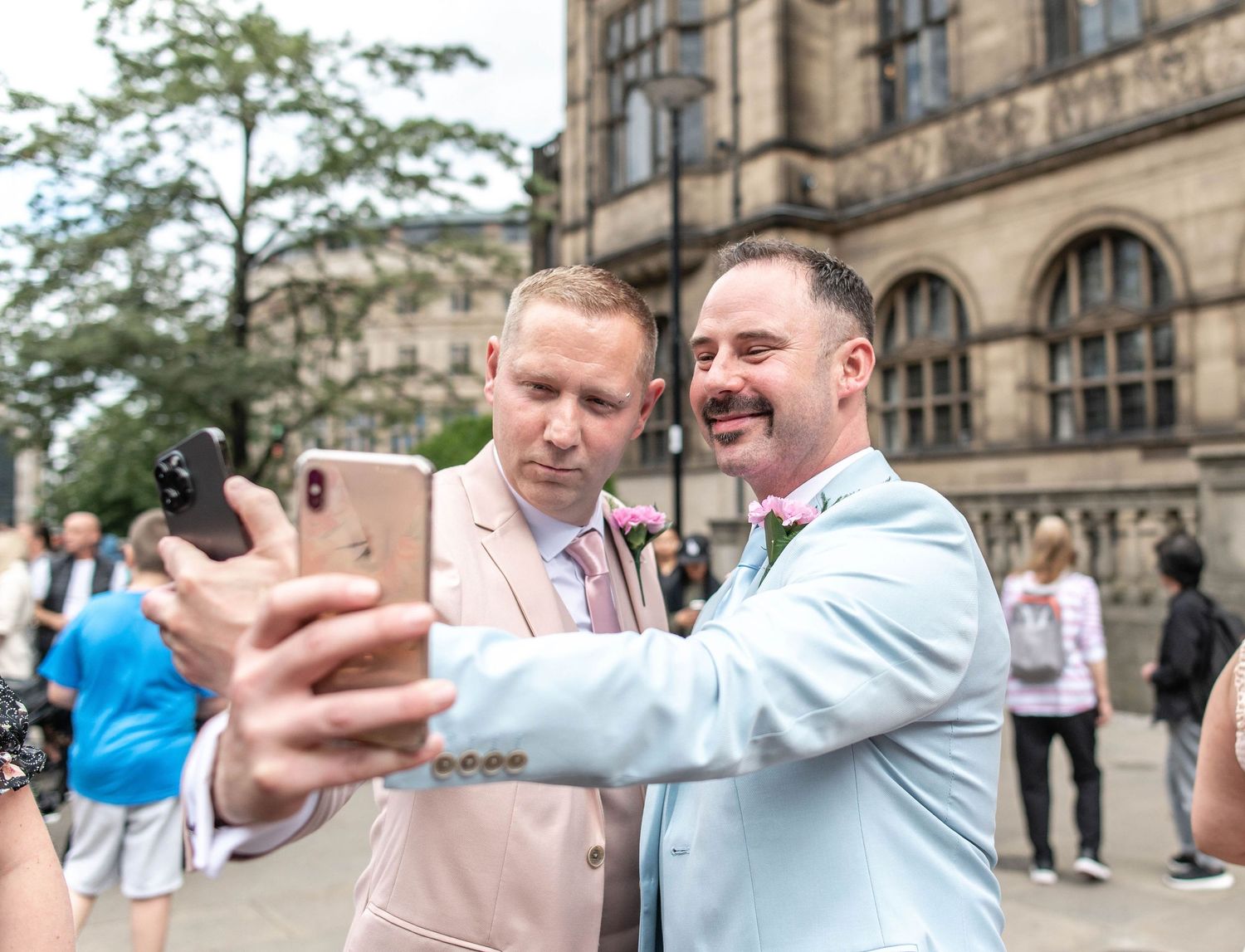 Two people in pastel suits taking selfie together outside historic building.