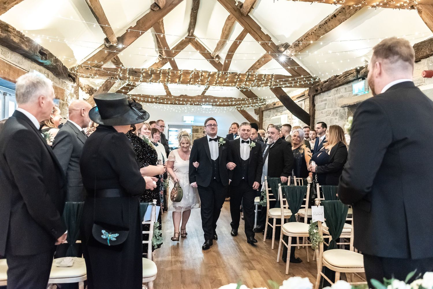 Wedding ceremony in progress inside a rustic barn venue with exposed wooden beams and natural lighting.