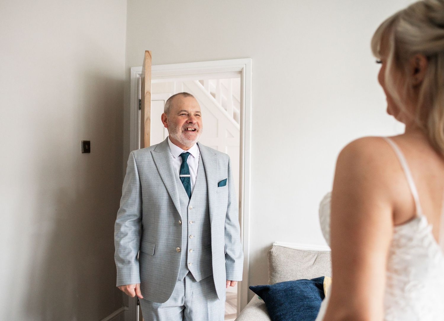 Emotional first look moment in light-filled room with grey suit and white dress.