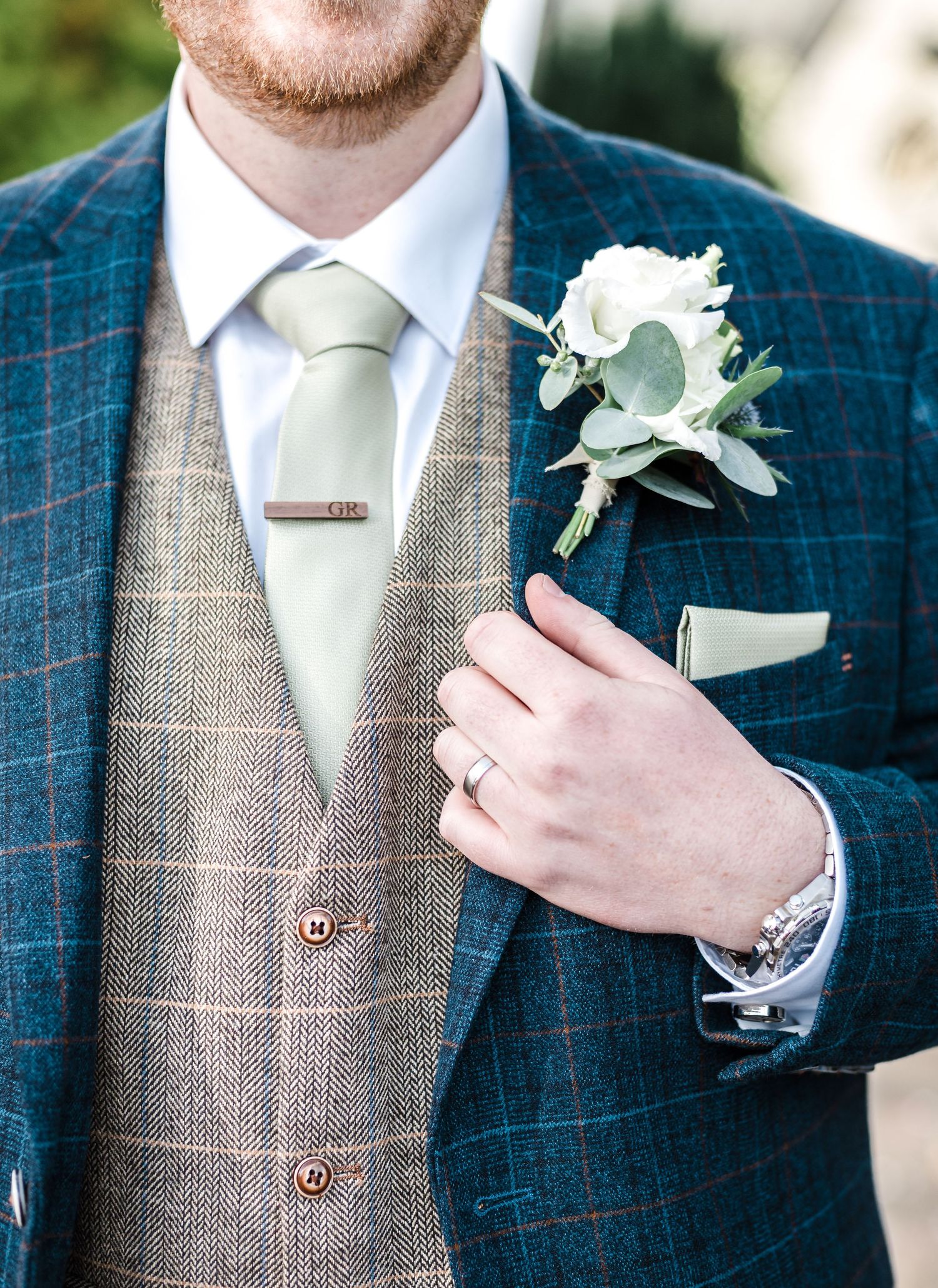 Close-up of groom's blue checkered suit with brown vest and white boutonniere.
