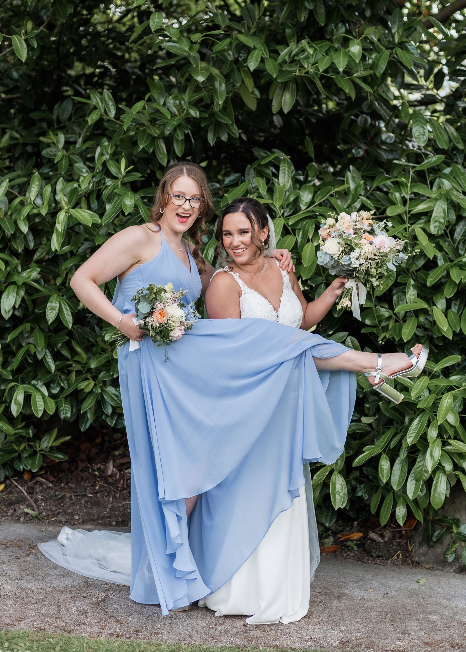 Joyful outdoor wedding photo with bridesmaids in light blue dresses and elegant floral bouquets.