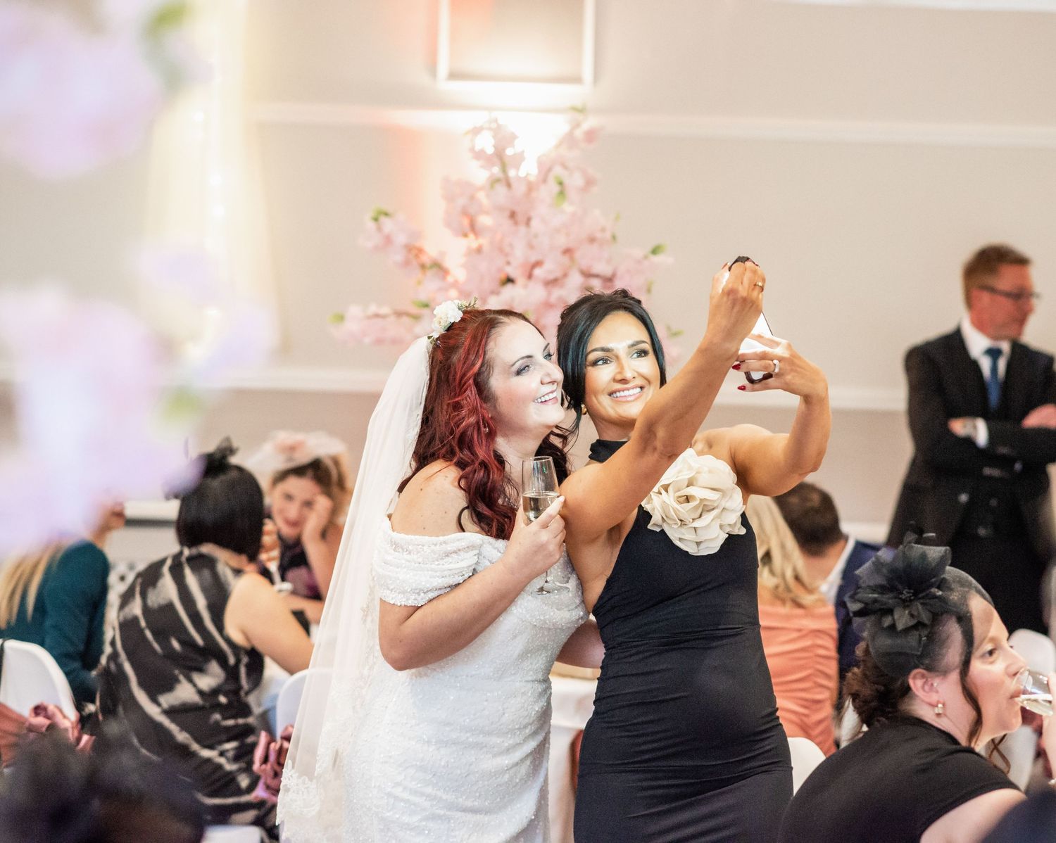 Wedding celebration selfie moment during indoor reception with pink floral decor.