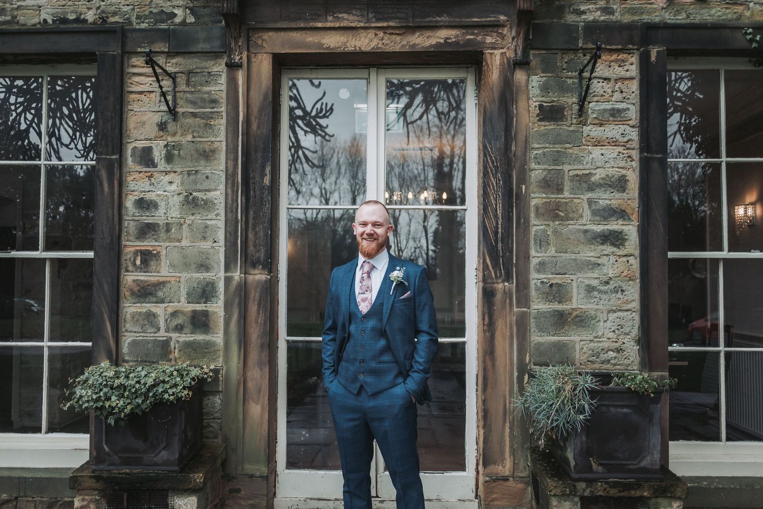 A suited figure stands in front of a stone building with traditional windows.