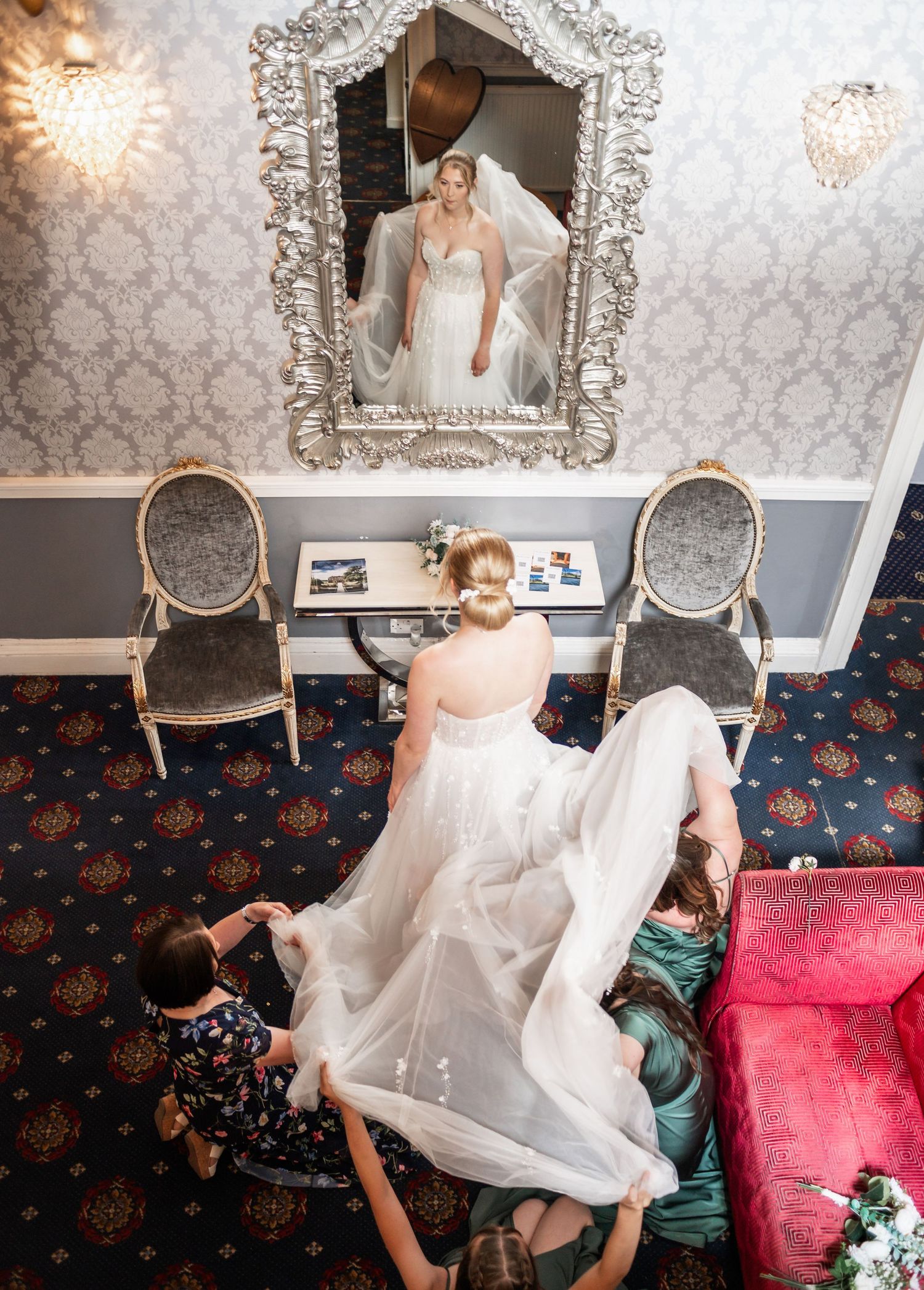 Wedding dress preparation moment reflected in an ornate silver mirror.