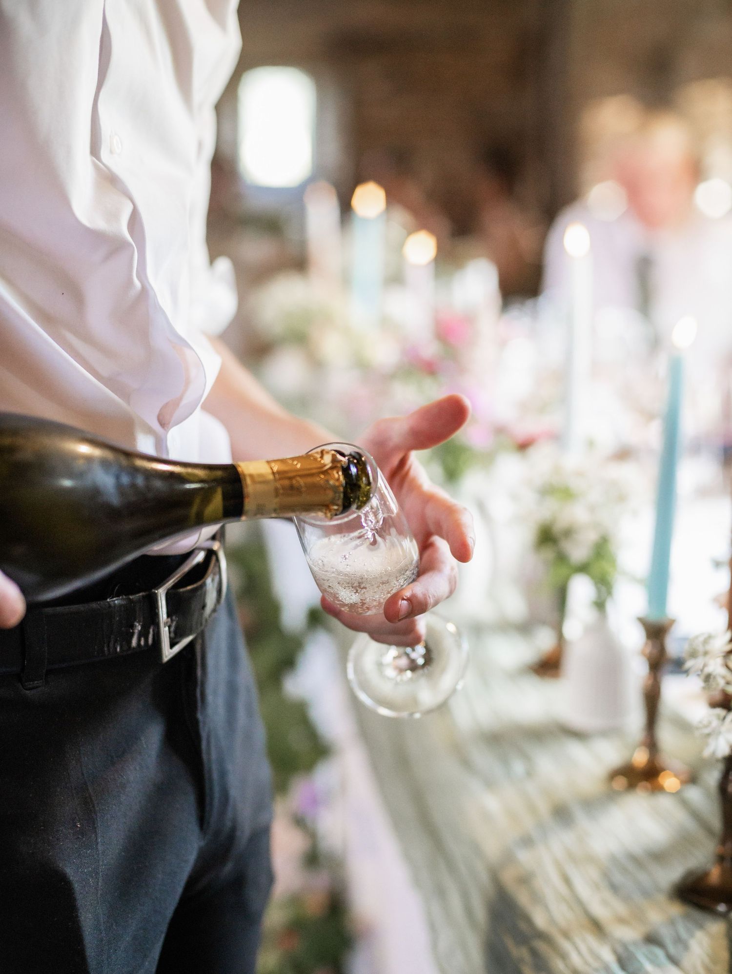 Server pouring champagne into a glass at an elegant wedding reception table.