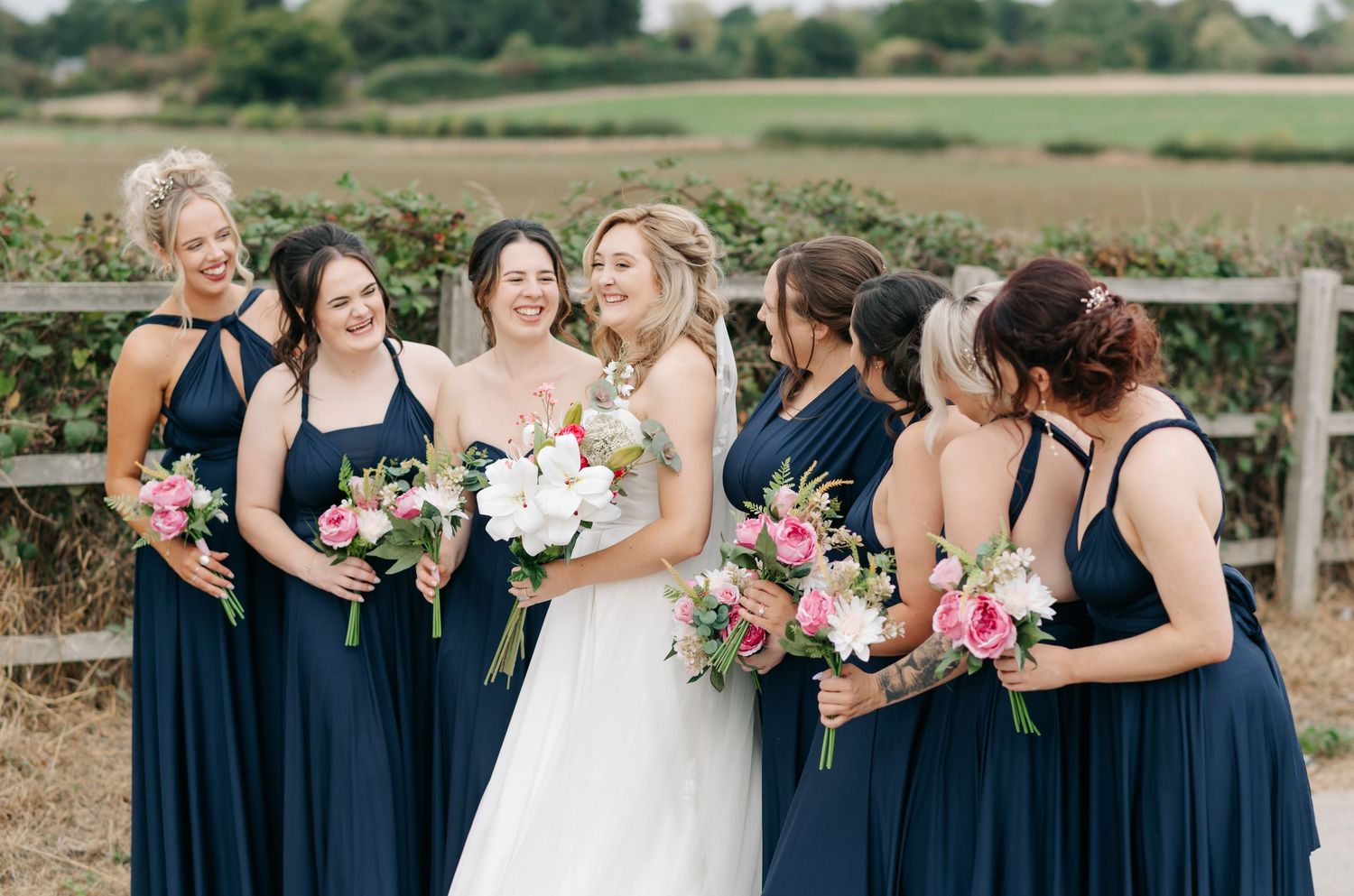Bridesmaids in navy dresses gather around bride for outdoor wedding photos.