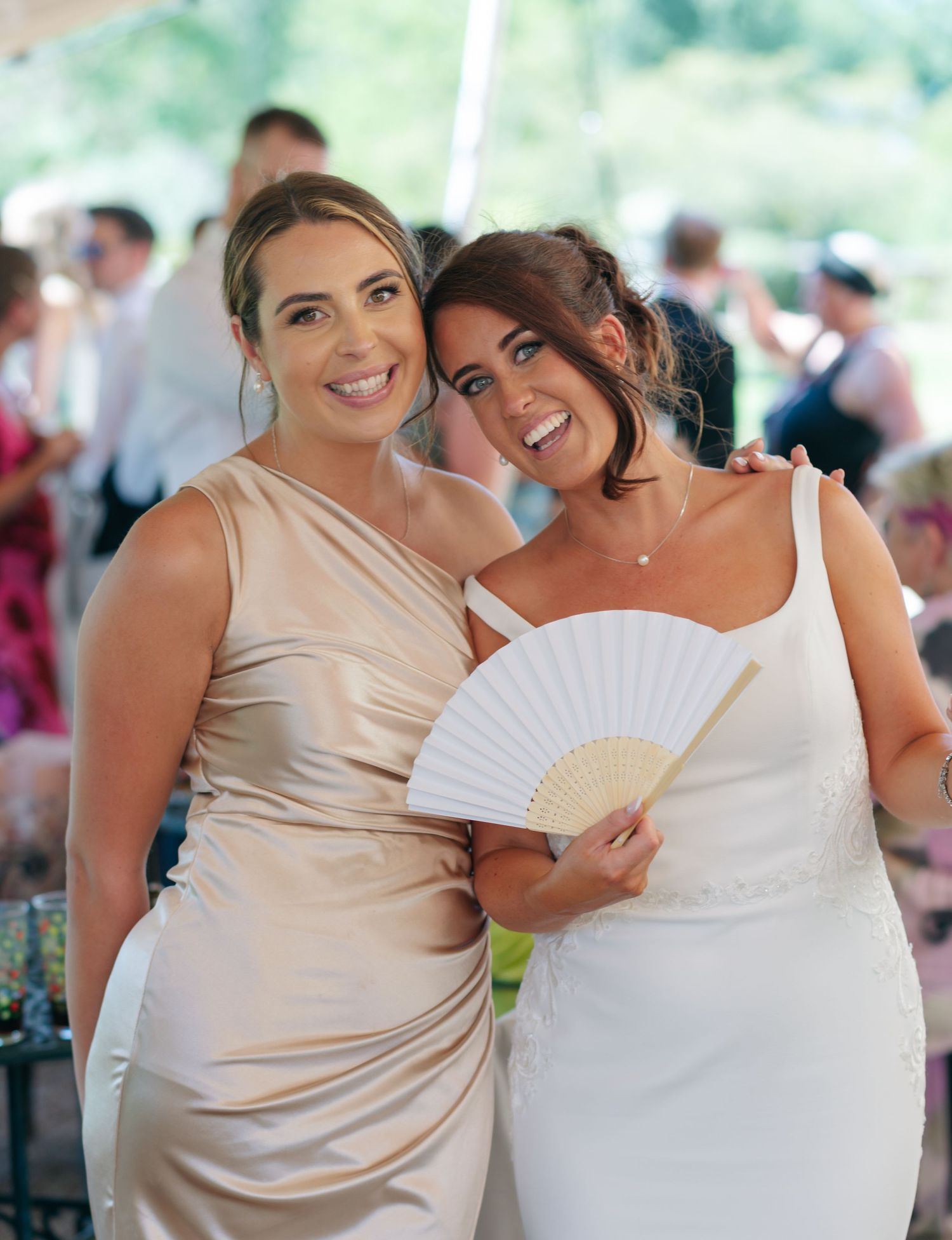 Wedding party members pose with decorative fans during outdoor summer celebration.