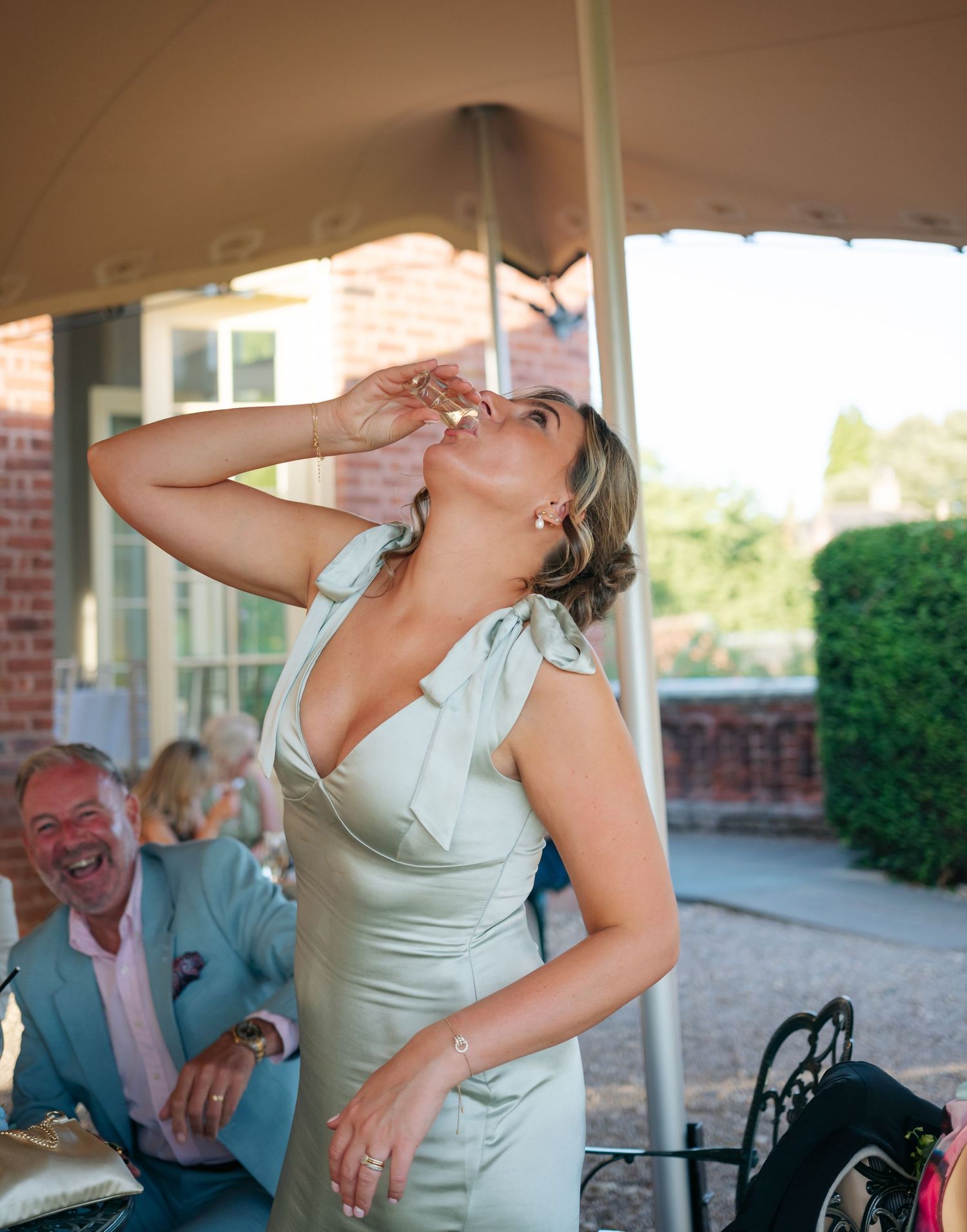 A person in a sage green dress laughs joyfully during outdoor celebrations.