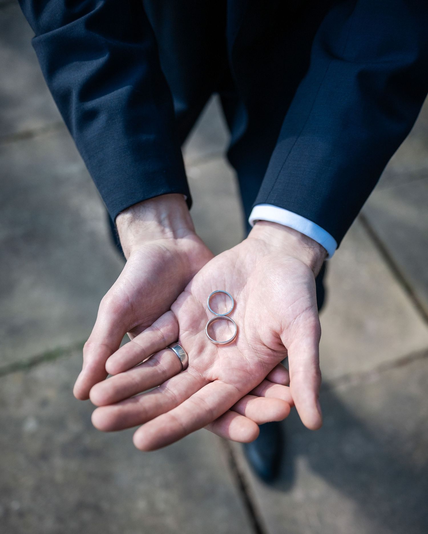 Wedding rings held delicately in outstretched palms against a dark background.