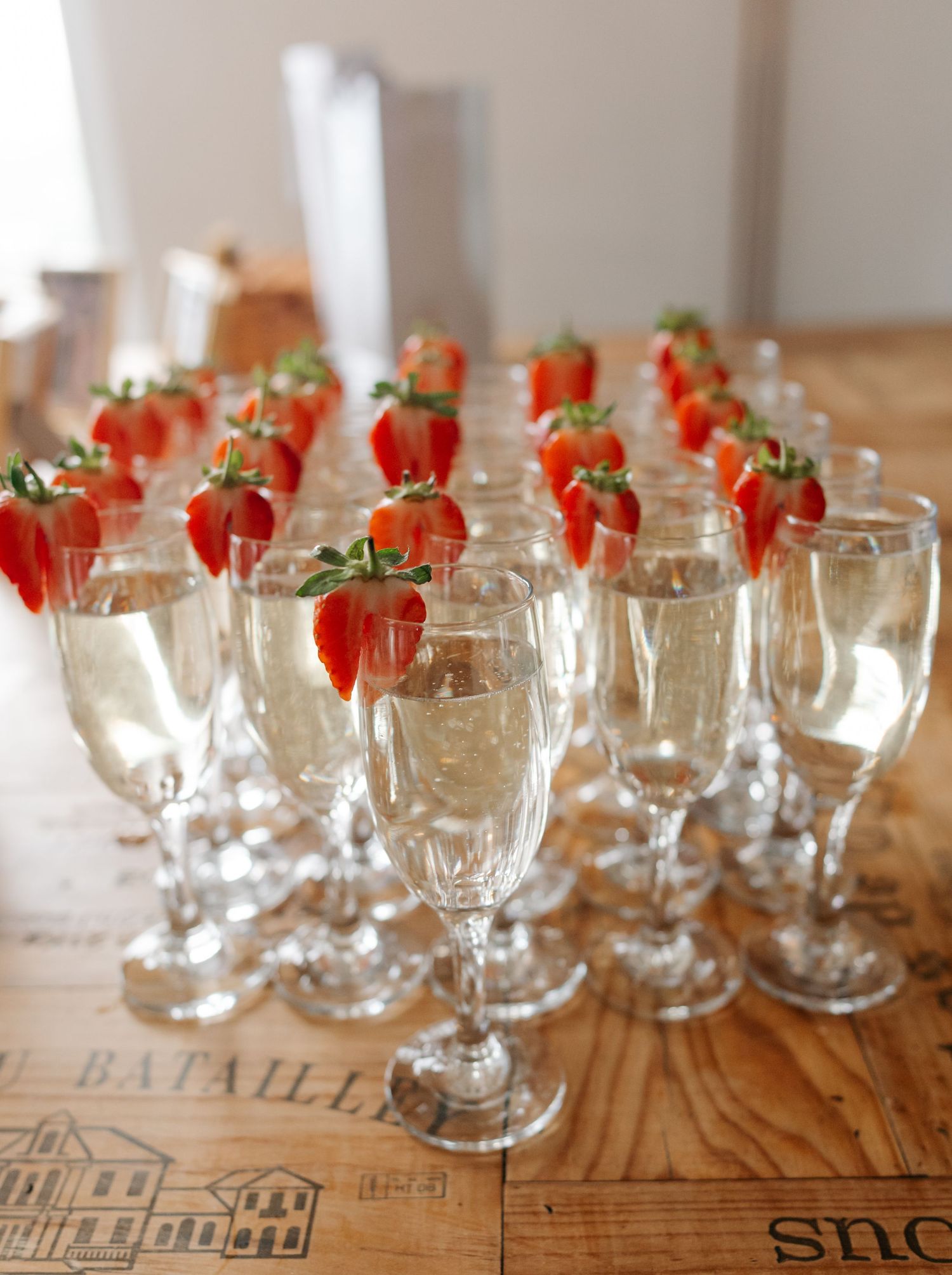 Elegant champagne flutes garnished with fresh strawberries arranged on a rustic wooden surface.