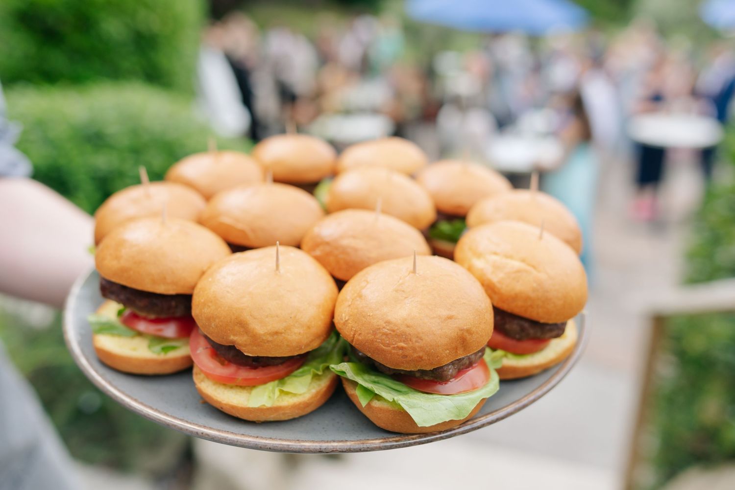 Fresh hamburger sliders arranged on serving plates at an outdoor event.