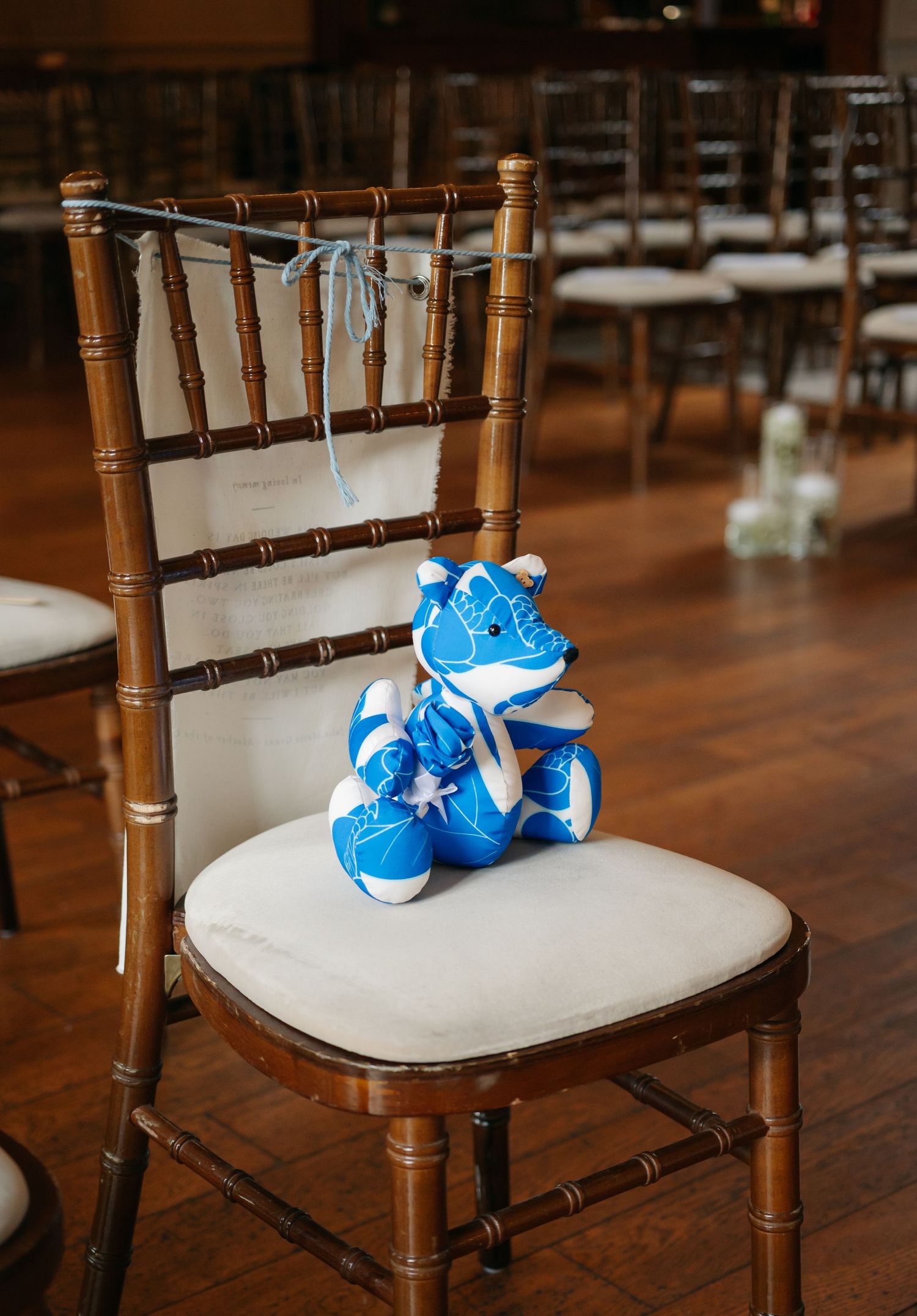 Blue baby shoes rest on a wooden Chiavari chair with cream cushioning at a wedding venue.