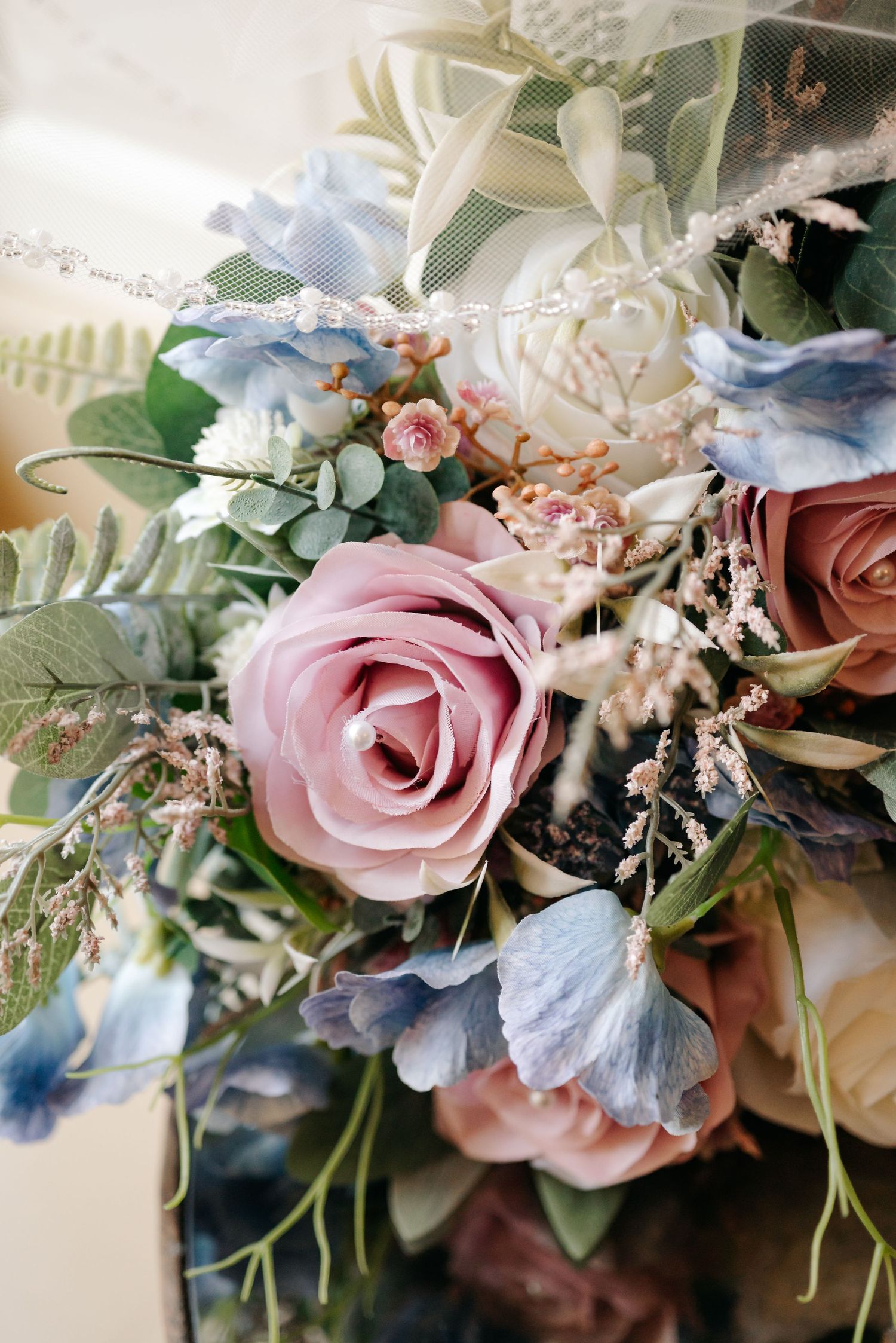 Close-up of a wedding bouquet featuring dusty pink roses, blue hydrangeas, and greenery with delicate details.