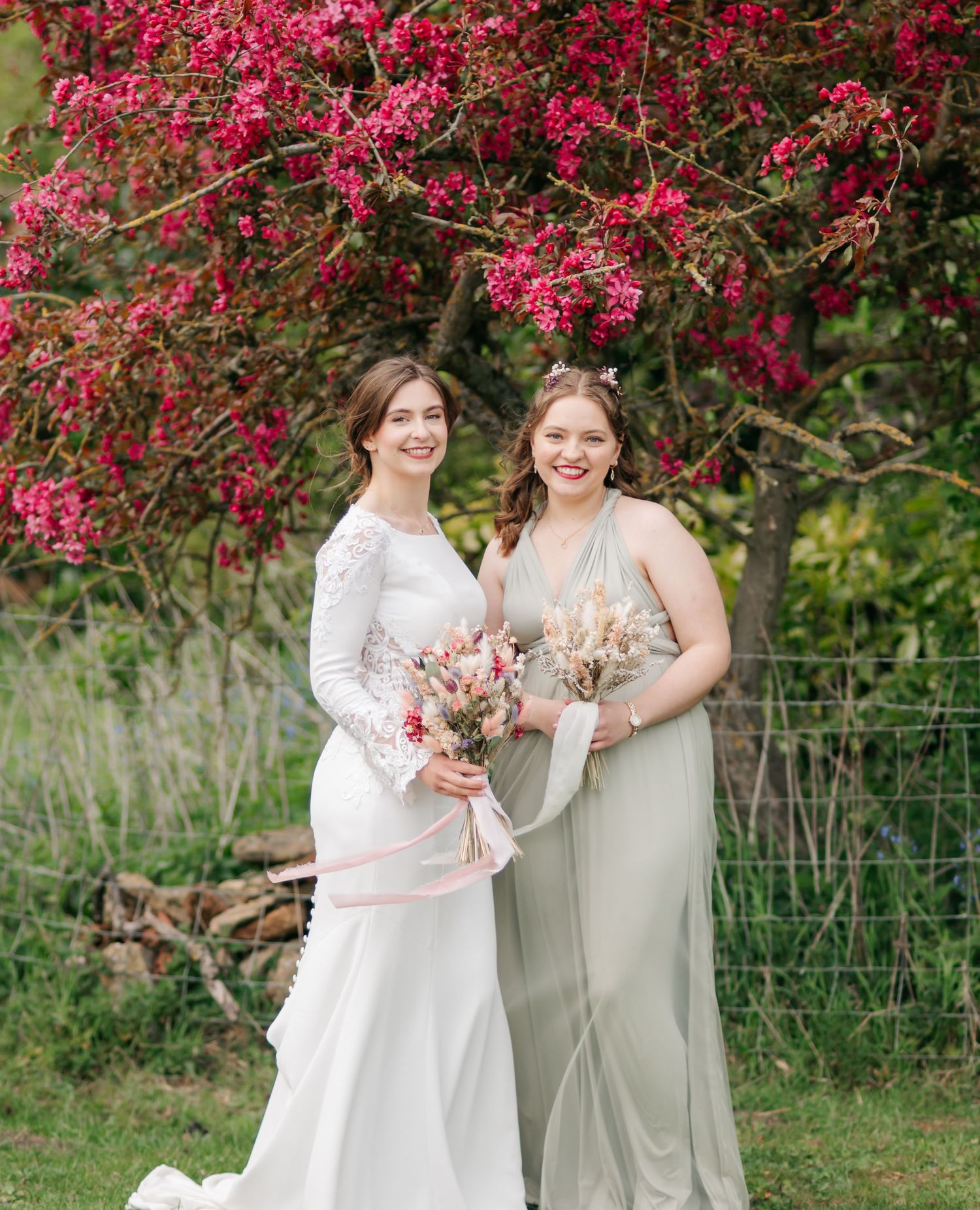 Wedding party poses in front of vibrant pink flowering trees during spring celebrations.