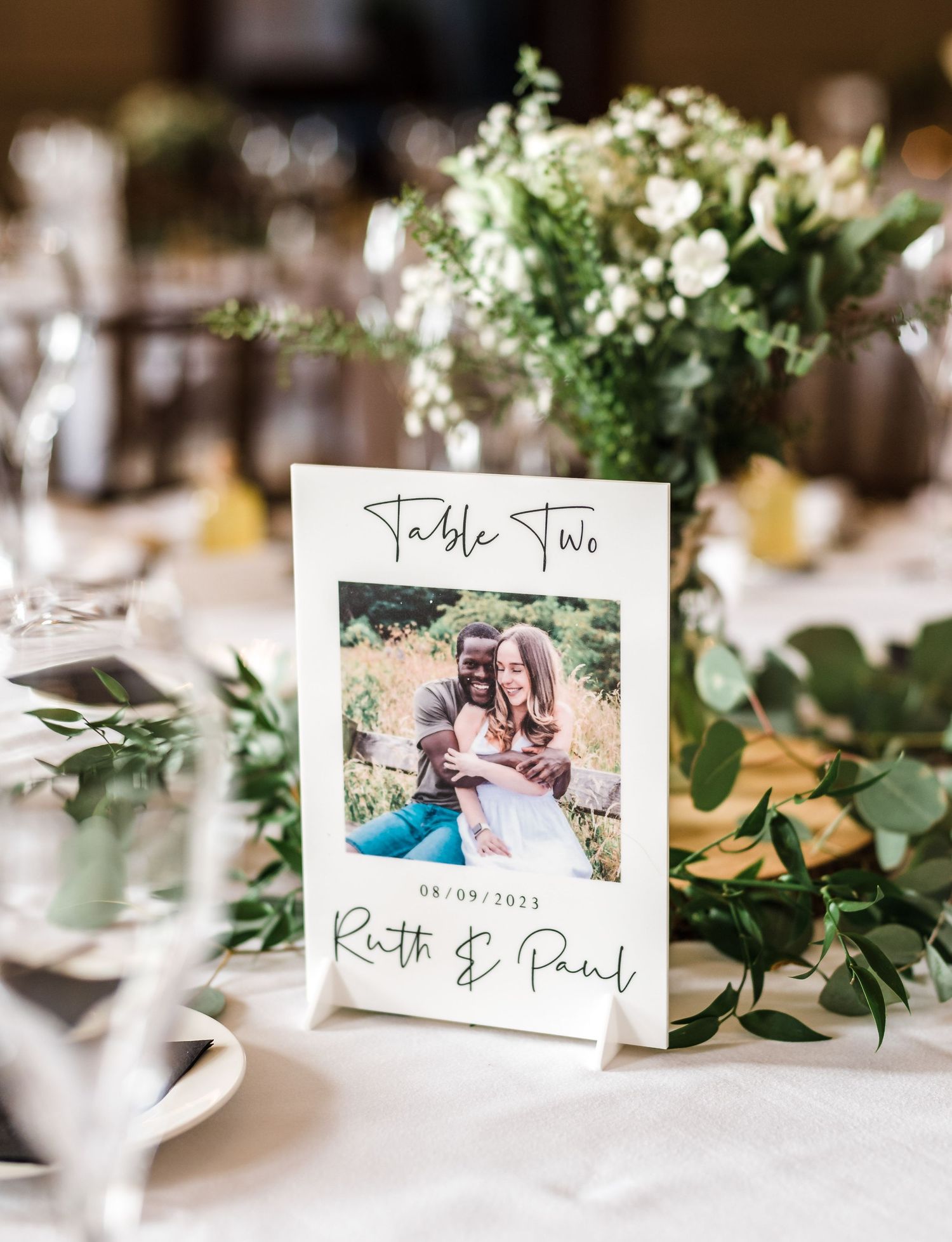 An elegant table setting with a floral centerpiece and framed photo table number.