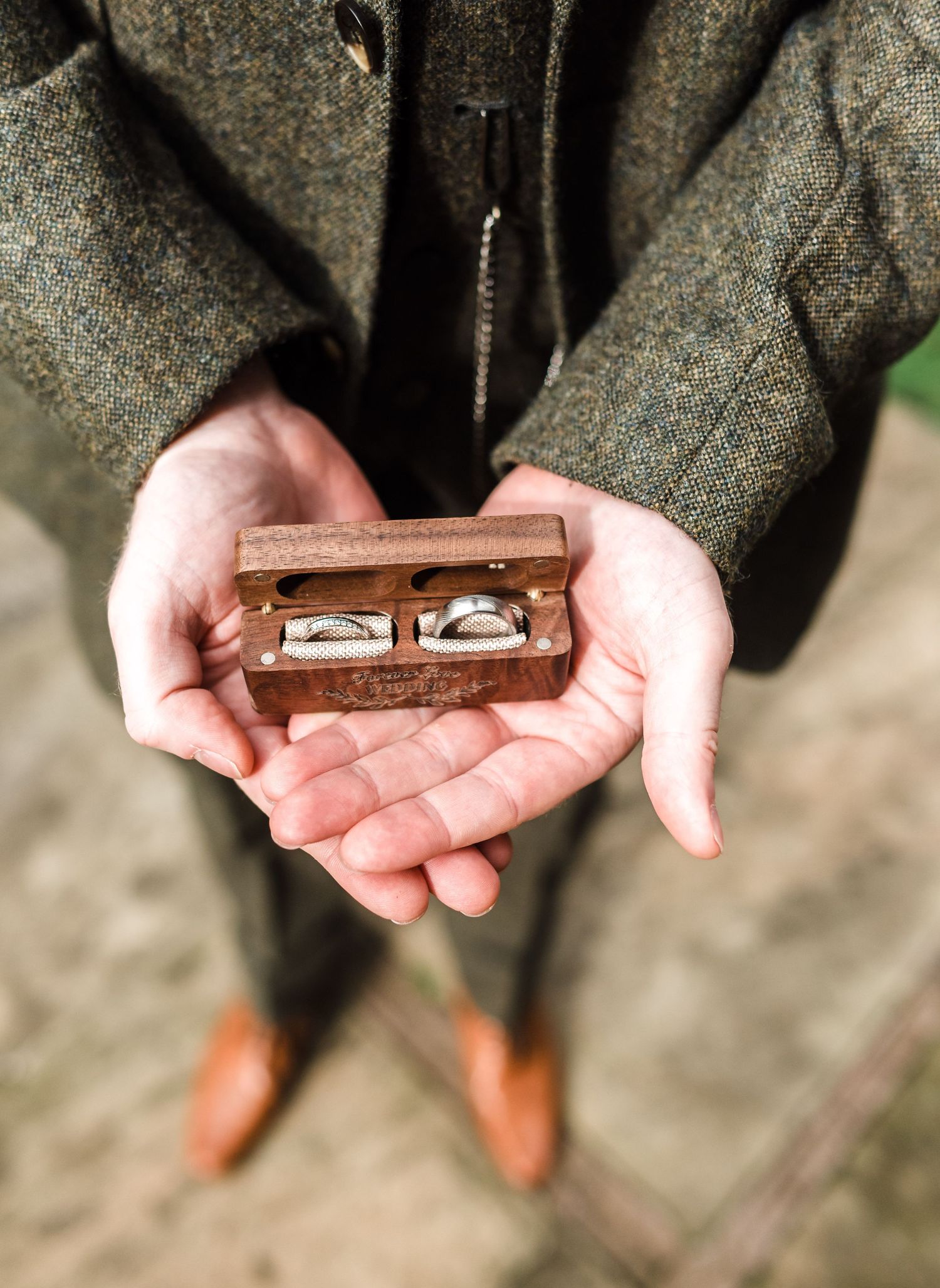 Hands holding wooden ring box with wedding bands inside.