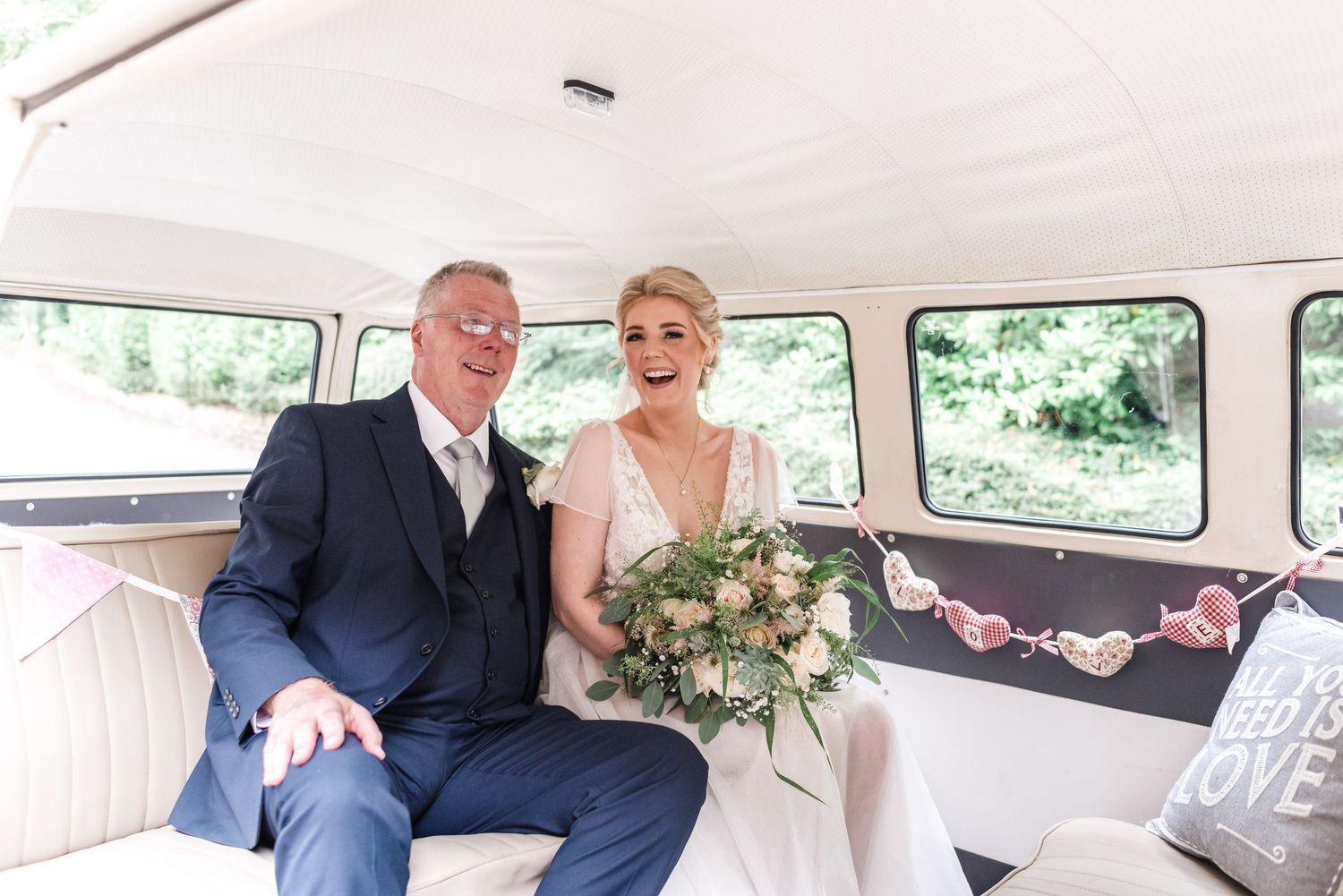 A couple rides in a vintage white wedding car decorated with love banners.