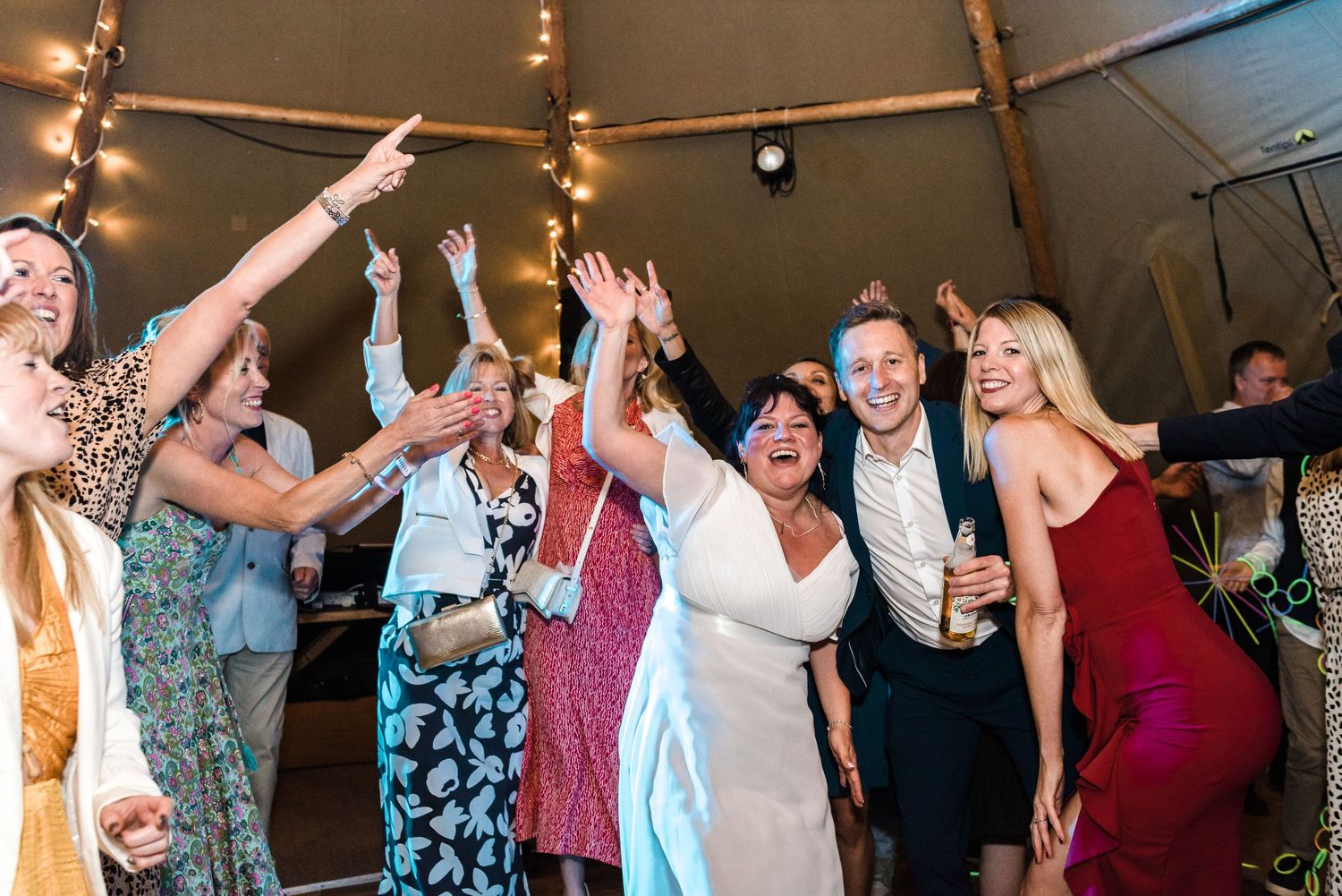 Group of wedding guests dancing and celebrating with hands raised.