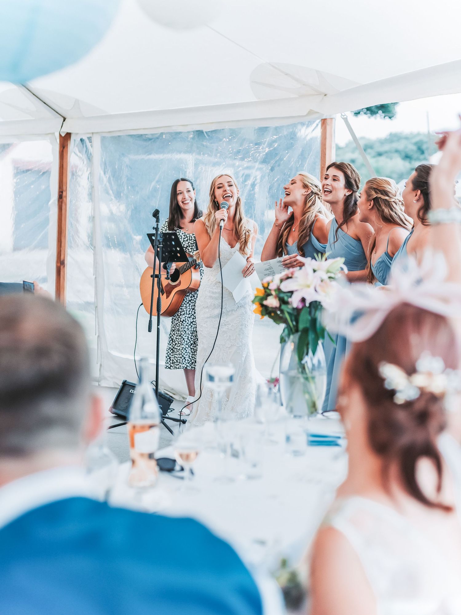 Musicians performing at a wedding reception under a white tent with blue decor.