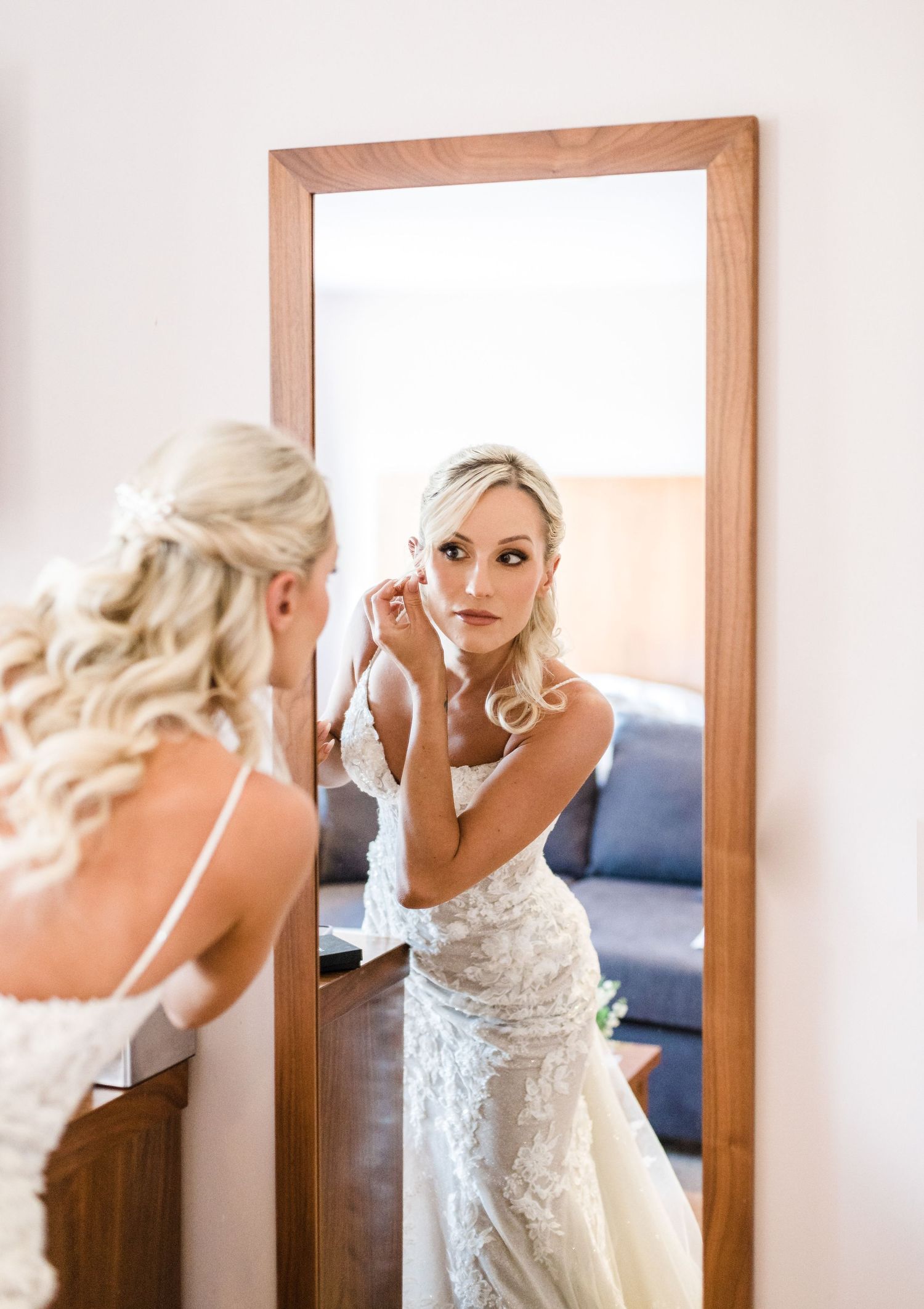 Reflection of bride getting ready in wooden framed mirror while applying makeup.