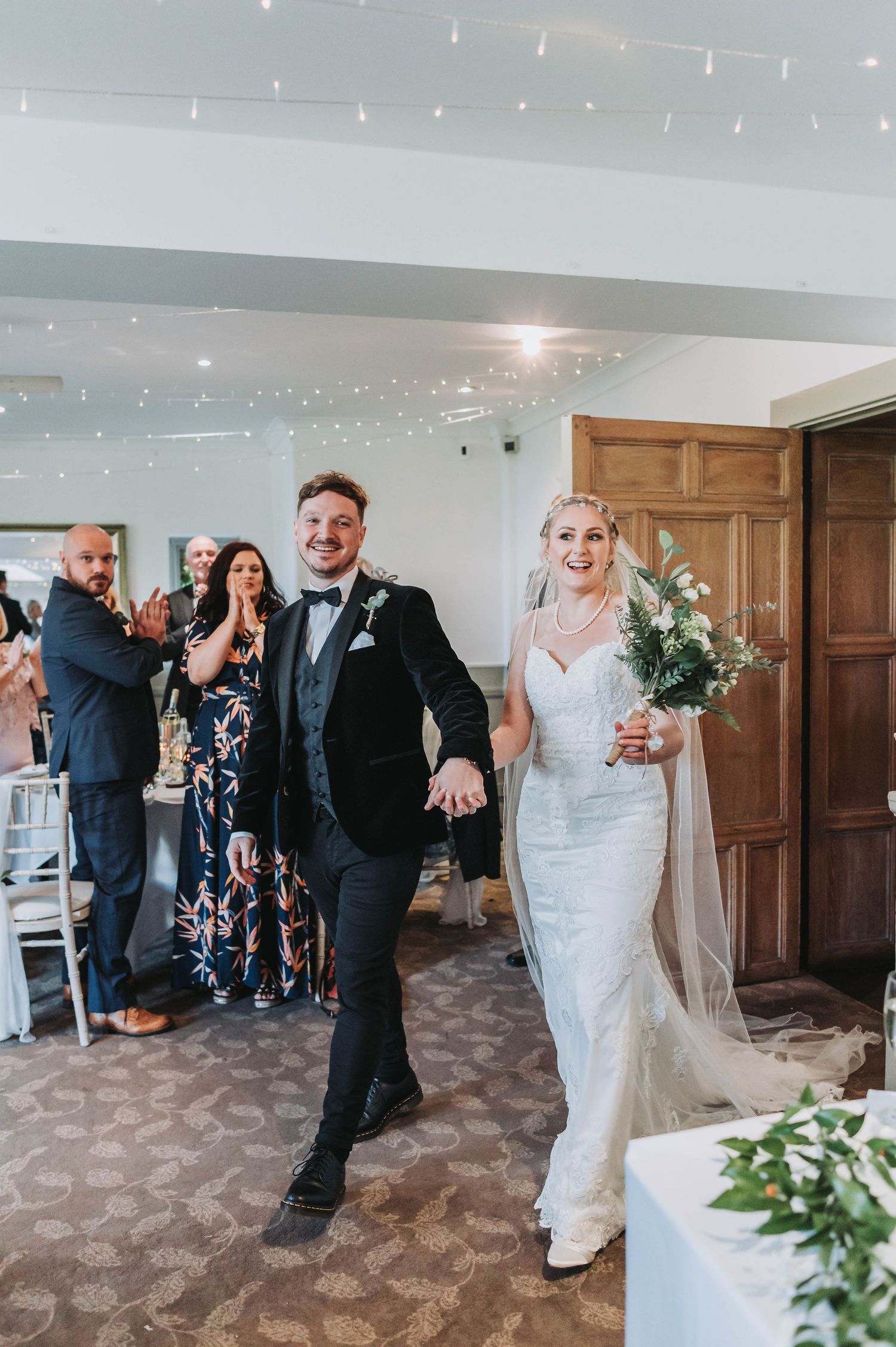 Wedding couple makes grand entrance into reception hall decorated with twinkling lights.