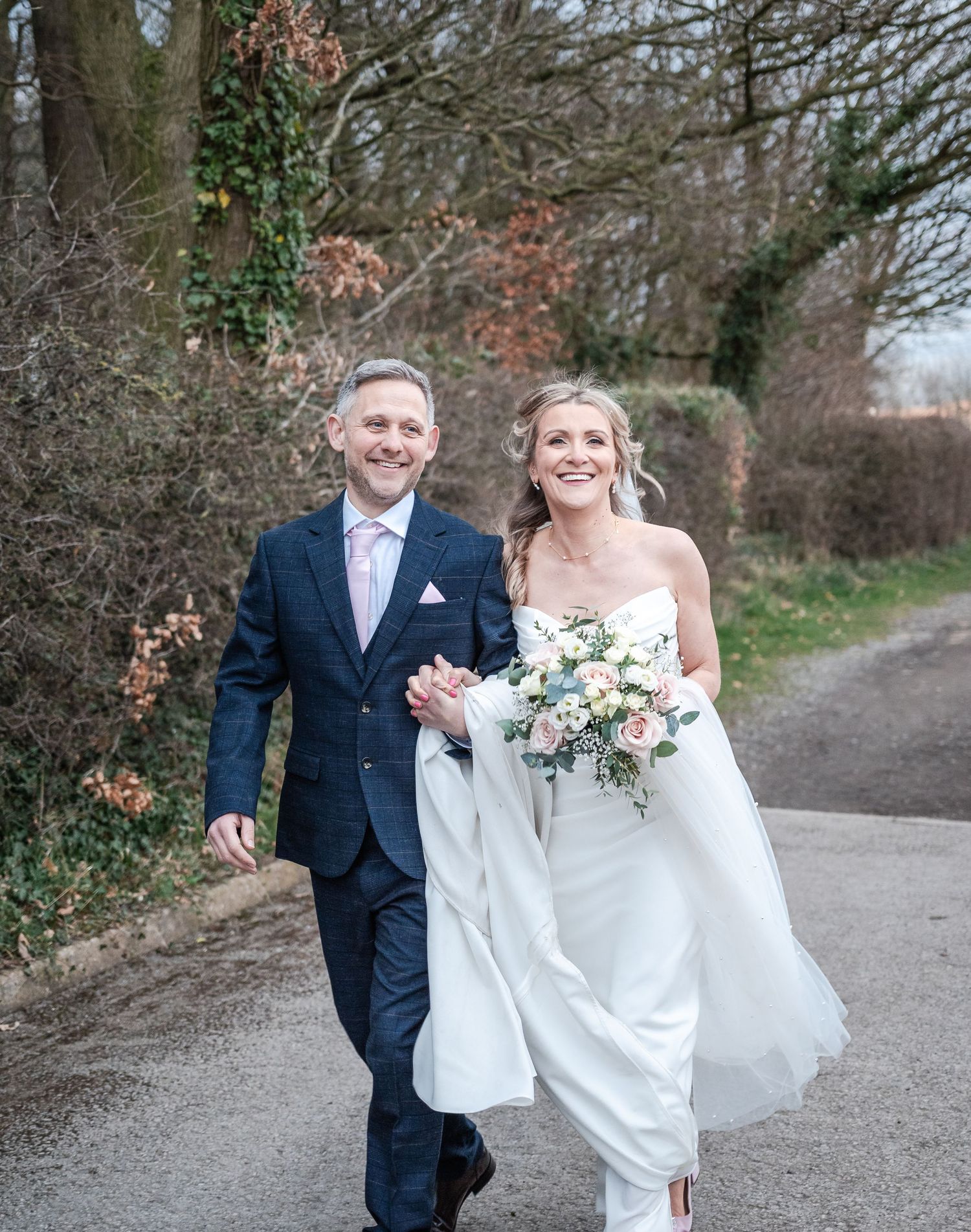 Couple walking and laughing together on country path during wedding portraits.