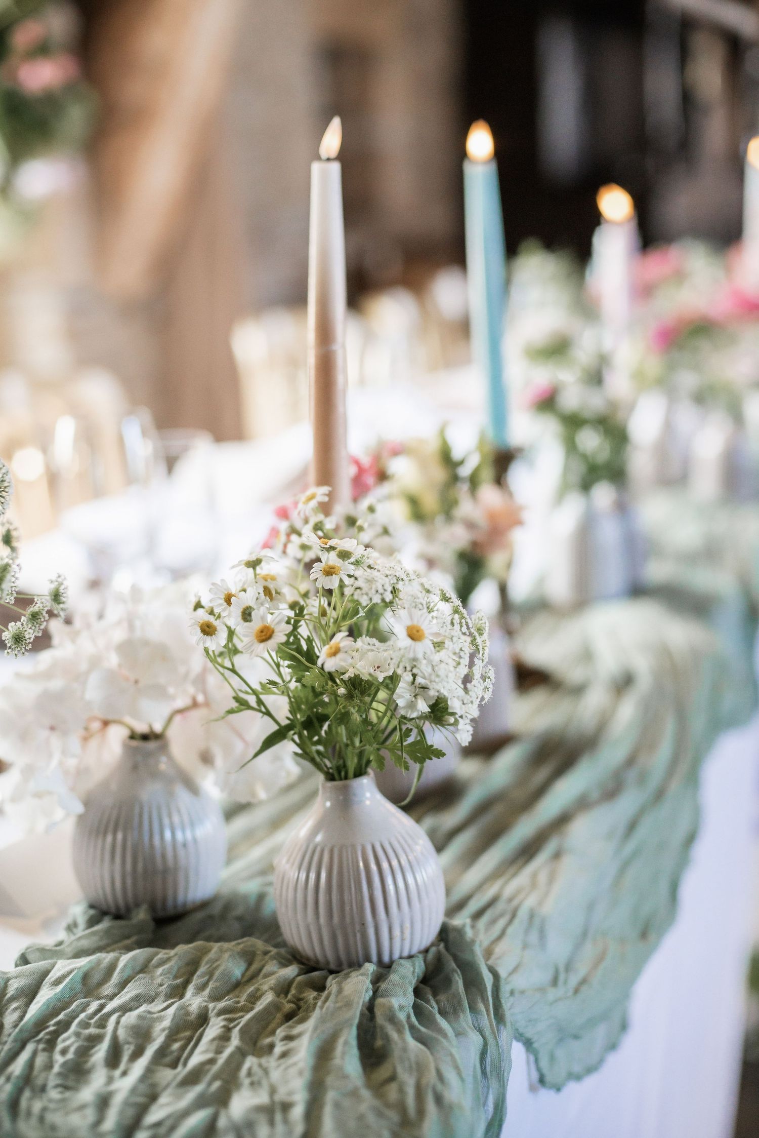 Table decor featuring taper candles and baby's breath in ribbed vases on sage green runner.