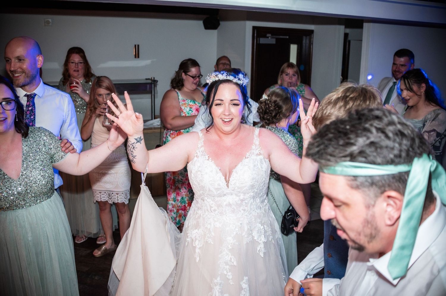Wedding guests dancing energetically in front of illuminated marquee letters at the reception.