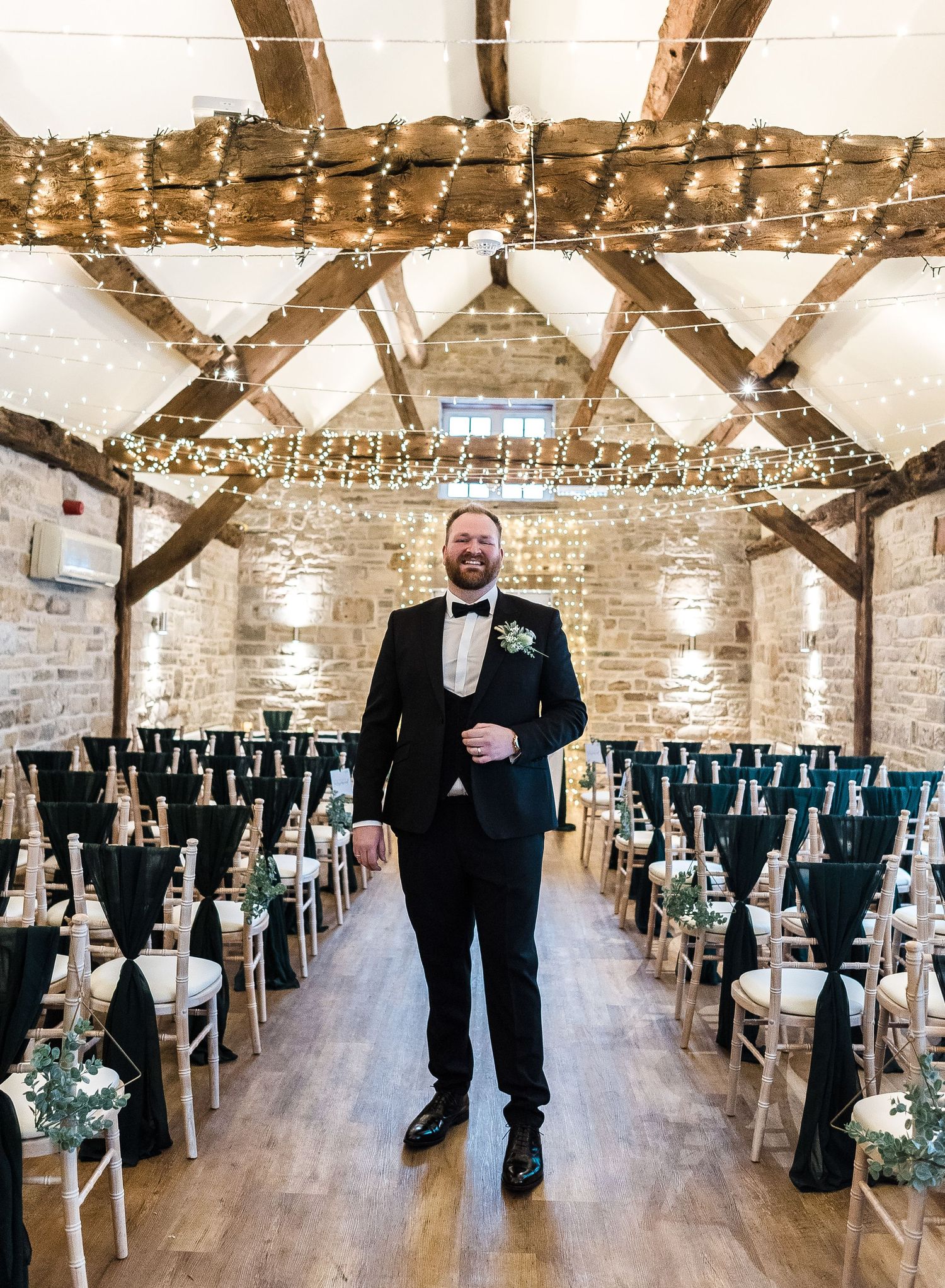 Rustic wedding ceremony space with exposed beams, fairy lights, and rows of chairs with teal accents.