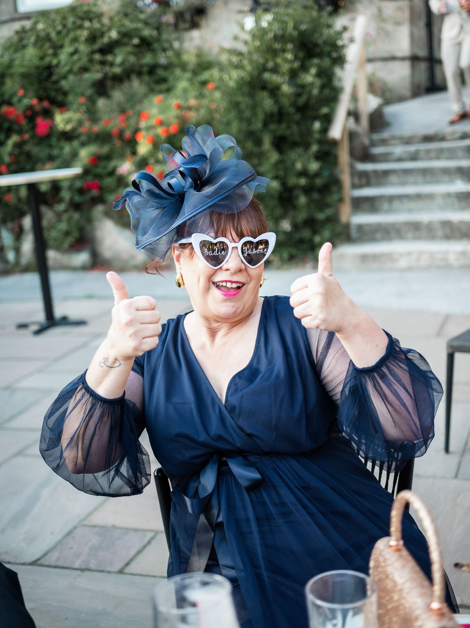 Wedding guest in navy dress and blue fascinator giving enthusiastic thumbs up.