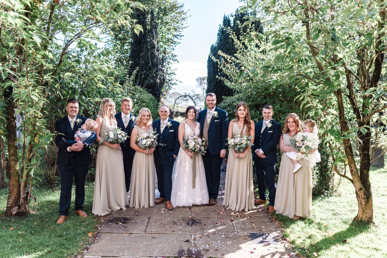 Wedding party in coordinated formal attire posed on garden path.
