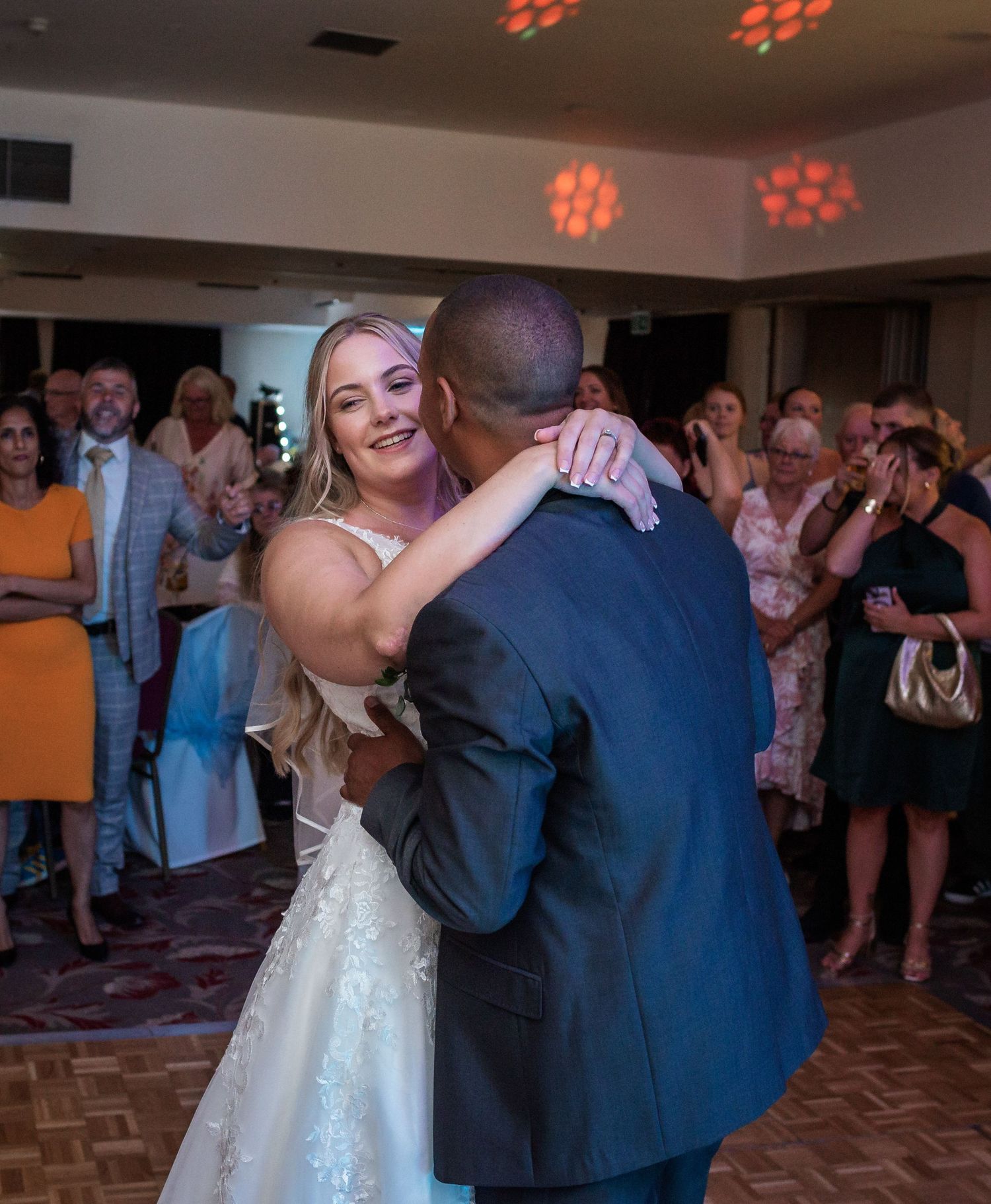 Newlyweds embrace during their first dance surrounded by wedding guests.