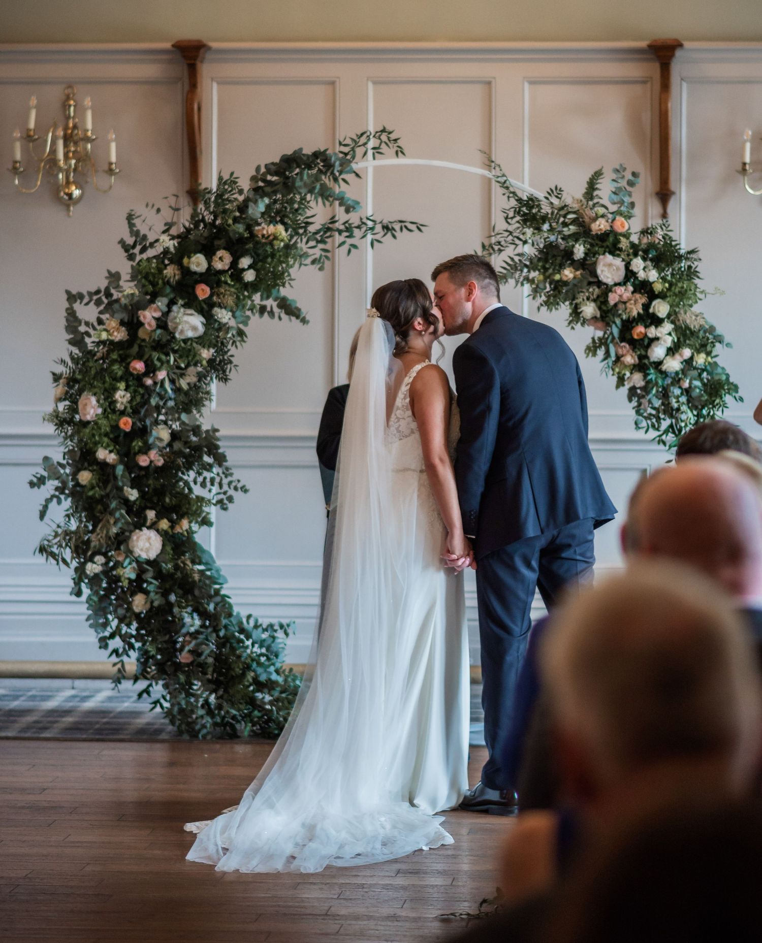 Wedding ceremony moment under a lush floral arch with pink and white blooms.