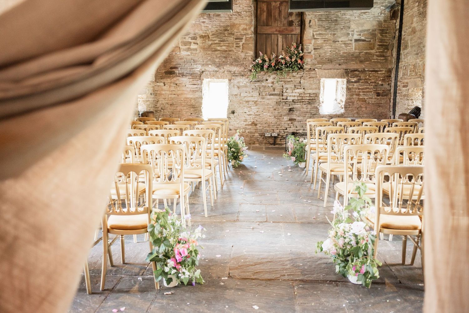 Rustic wedding ceremony setup with wooden chairs and floral aisle decorations in brick venue.