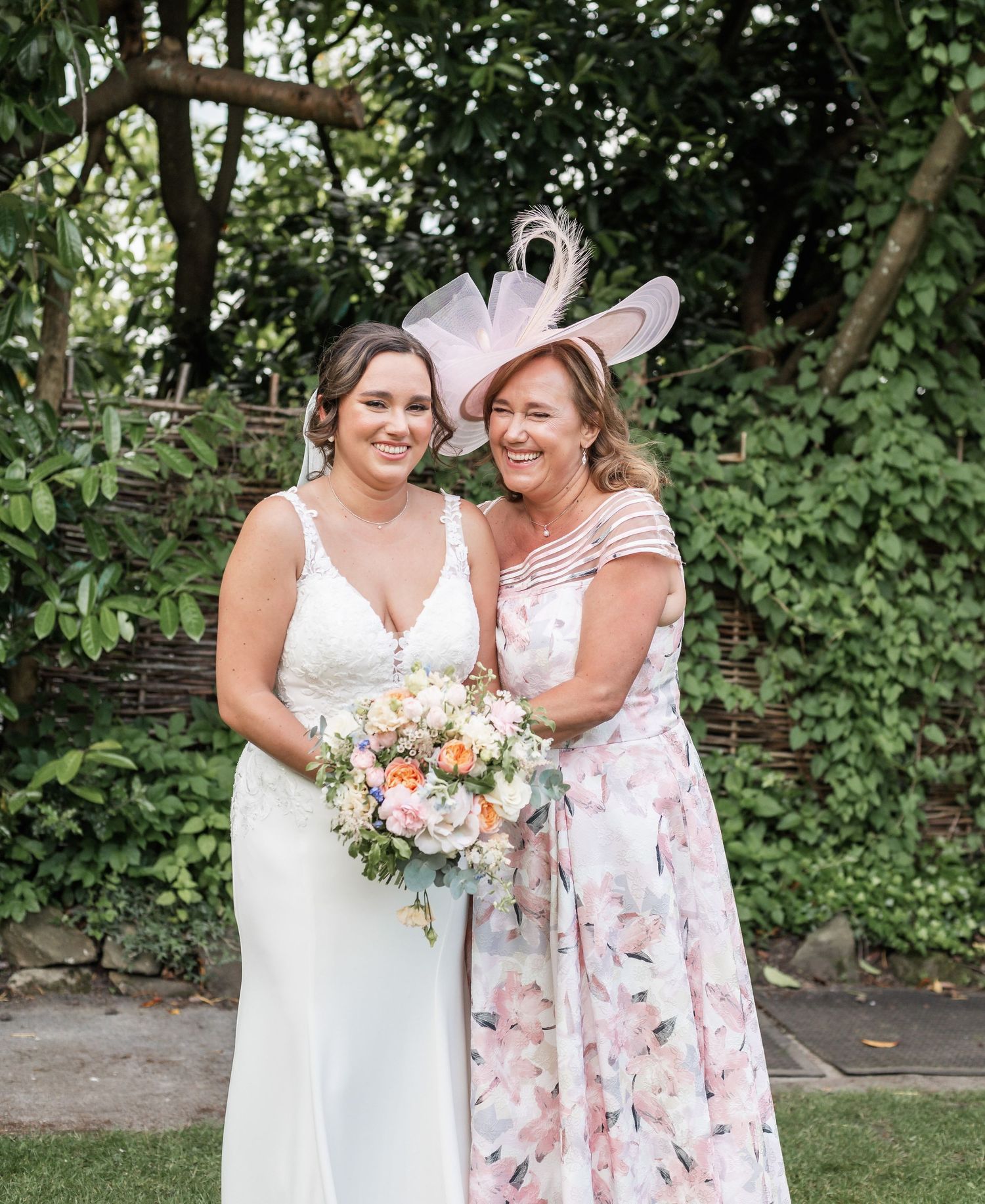 Outdoor garden wedding portrait featuring floral bouquet and pink fascinator.