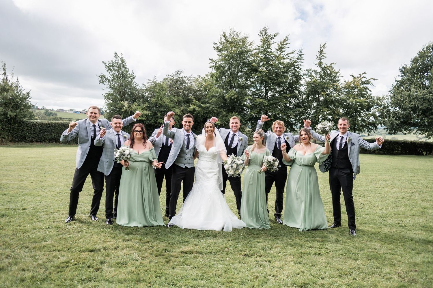 Wedding party in gray suits and mint green dresses posing together on grass.