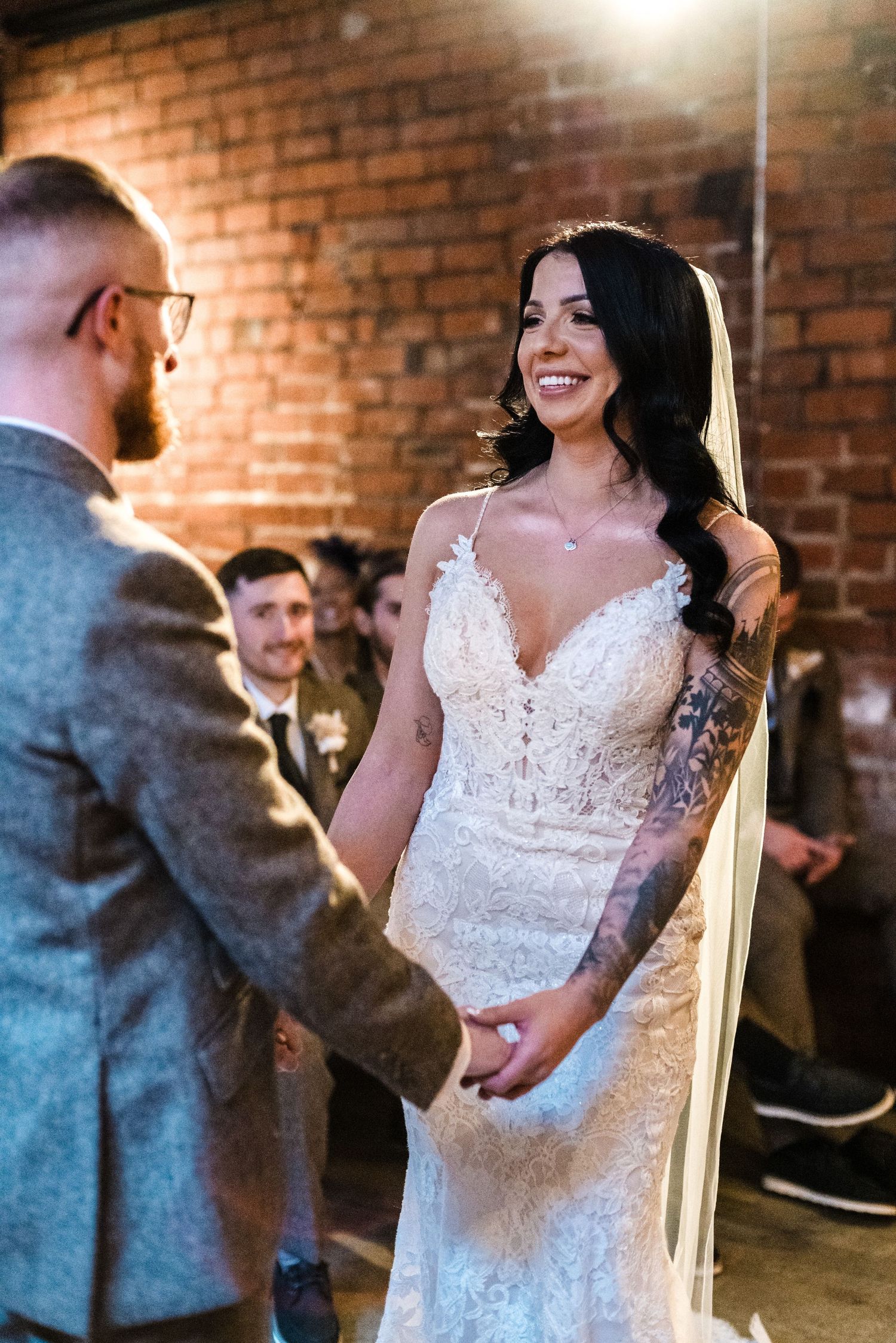 Bride in lace wedding dress exchanging vows in rustic brick venue.
